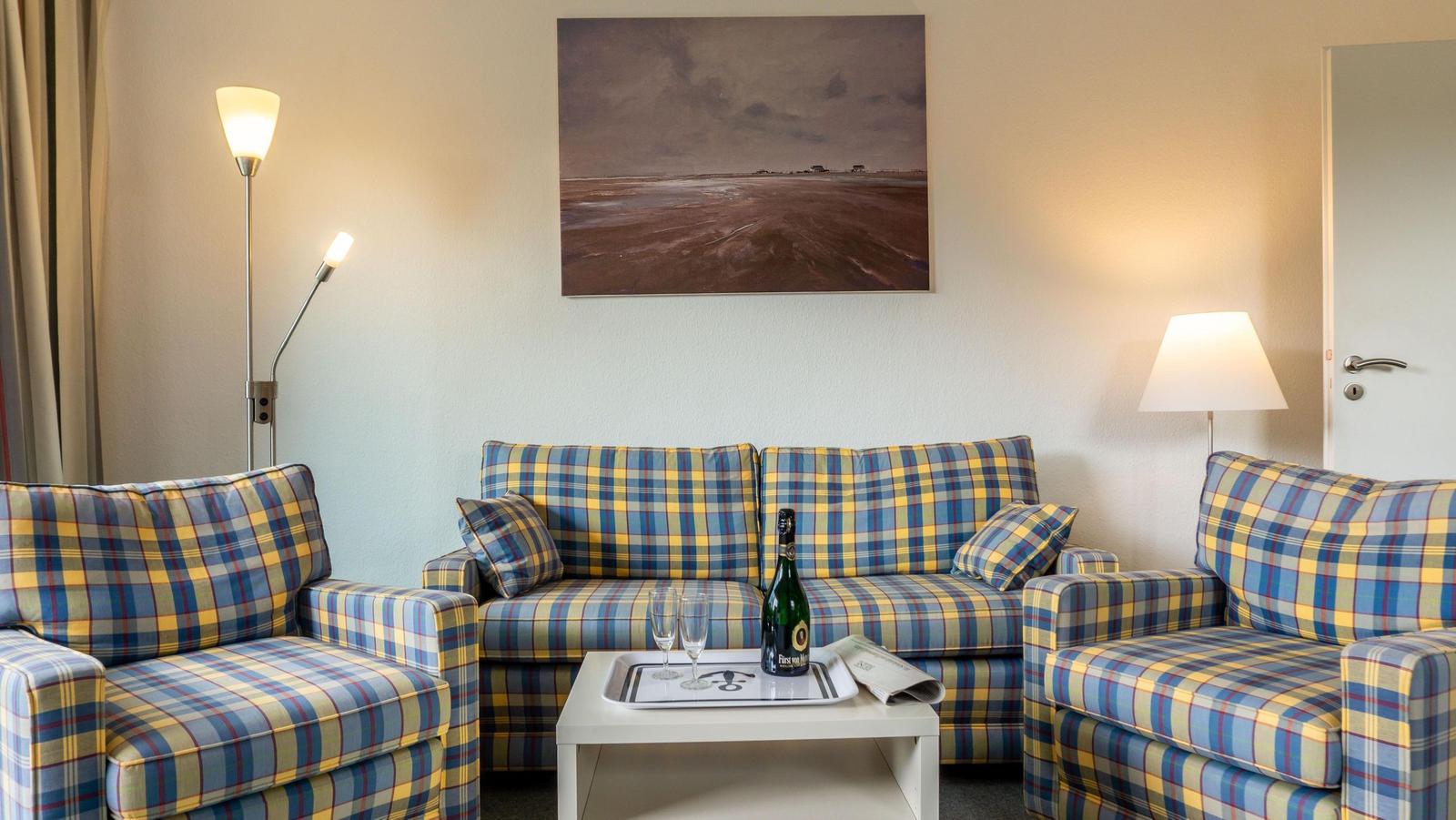 Wohnzimmer mit kariertem Sofa, Tisch mit Champagner und Wandbild.