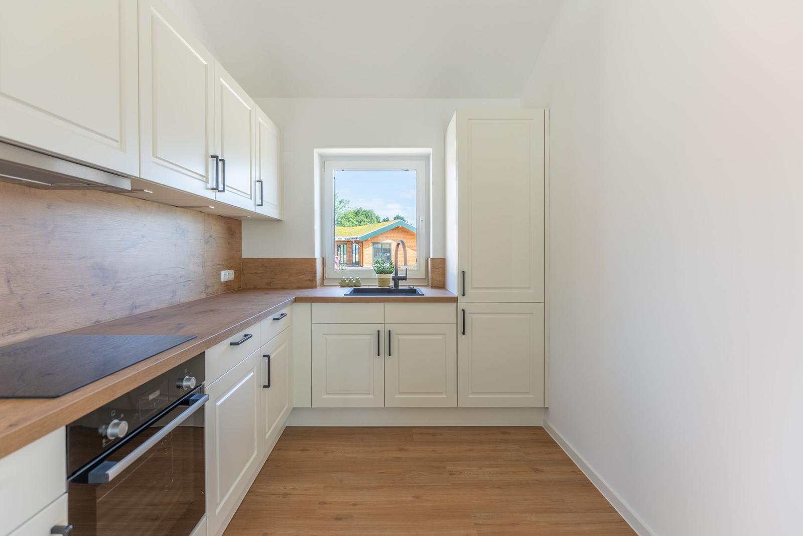 Küche mit weißen Schränken, Holzoberflächen und Fensterblick.