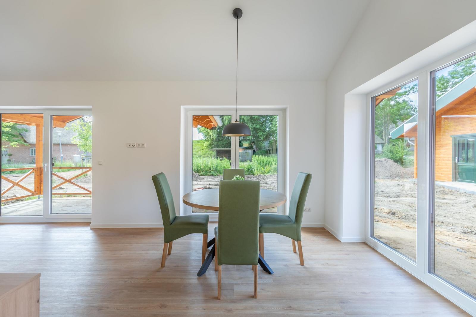 Esszimmer mit runden Tisch, grünen Stühlen und großen Fenstern zur Aussicht.