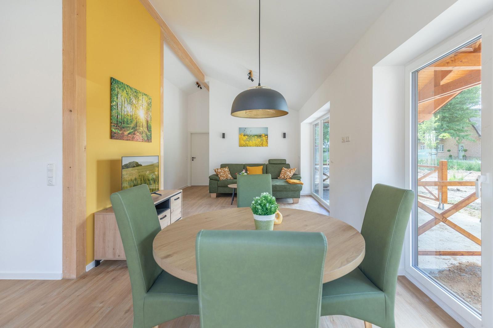 Essbereich mit runden Tisch und grünen Stühlen. Wohnbereich mit Sofa und Fensterblick.