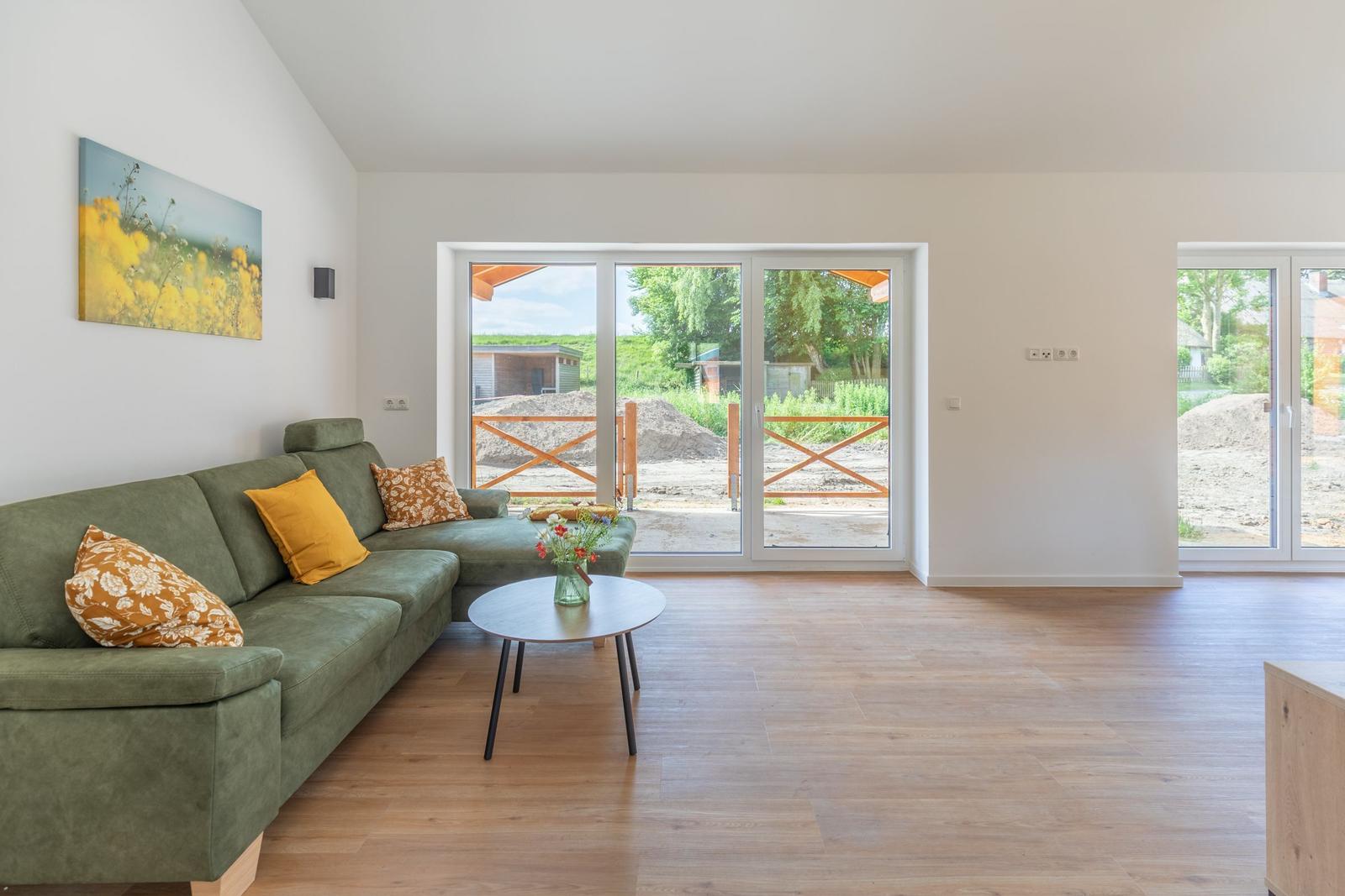 Grünes Sofa mit Kissen, Holzboden und Glastüren zur Terrasse.