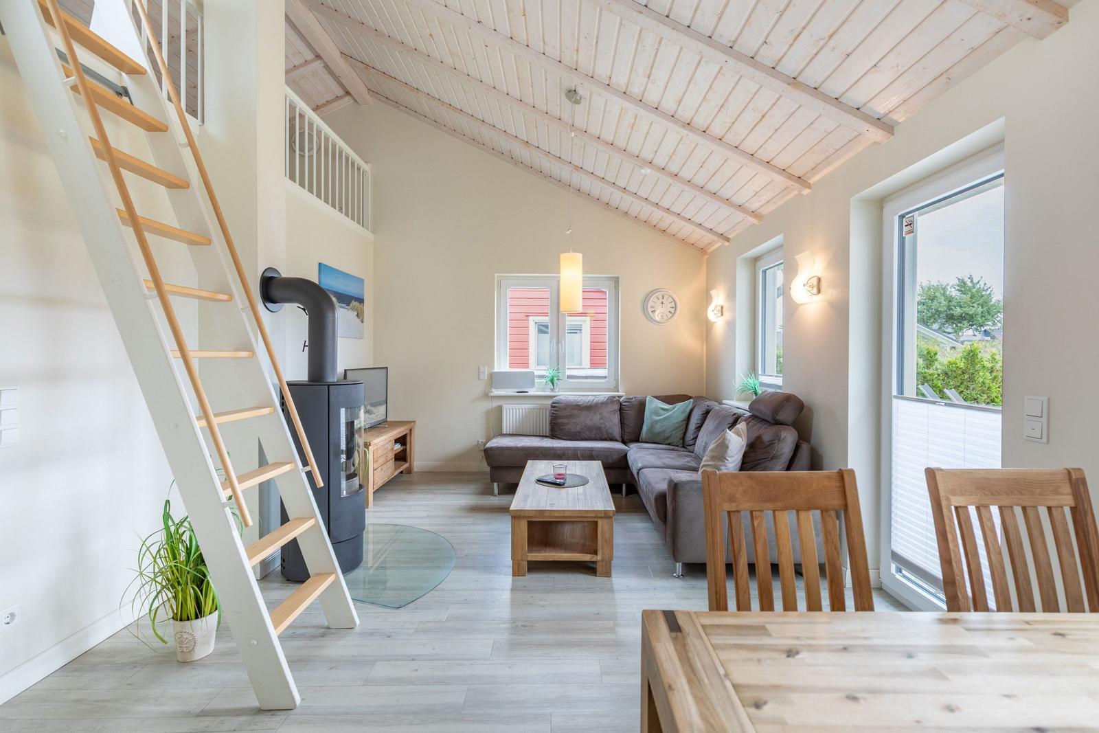 Wohn- und Essbereich mit Holztreppe und Kaminofen. Große Fenster und Balkon.