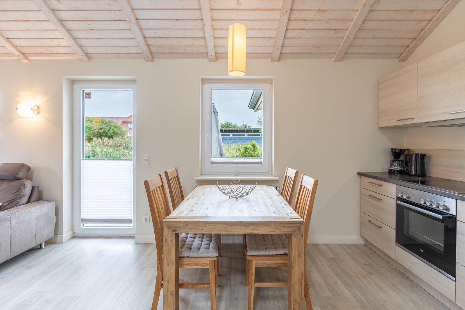Essbereich mit Holztisch, Stühlen und Küchenzeile. Durchgang zur Wohnfläche mit Sofa.