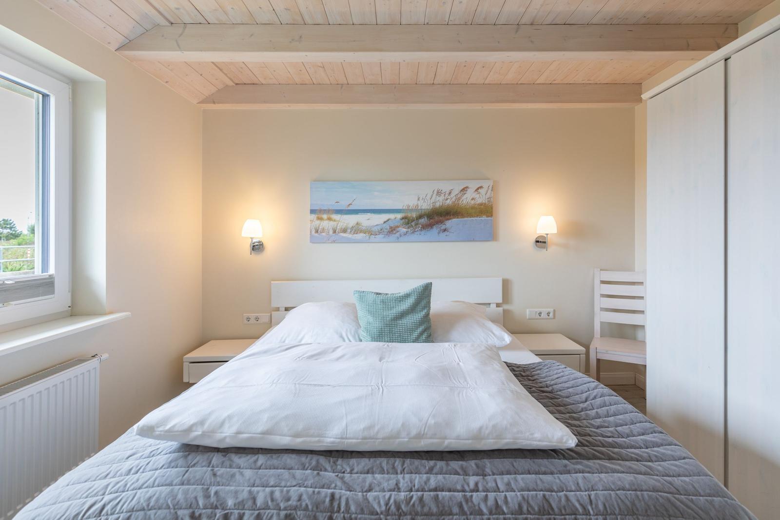 Schlafzimmer mit Bett, Nachttischen und Wandbild. Holzdecke und Fenster.