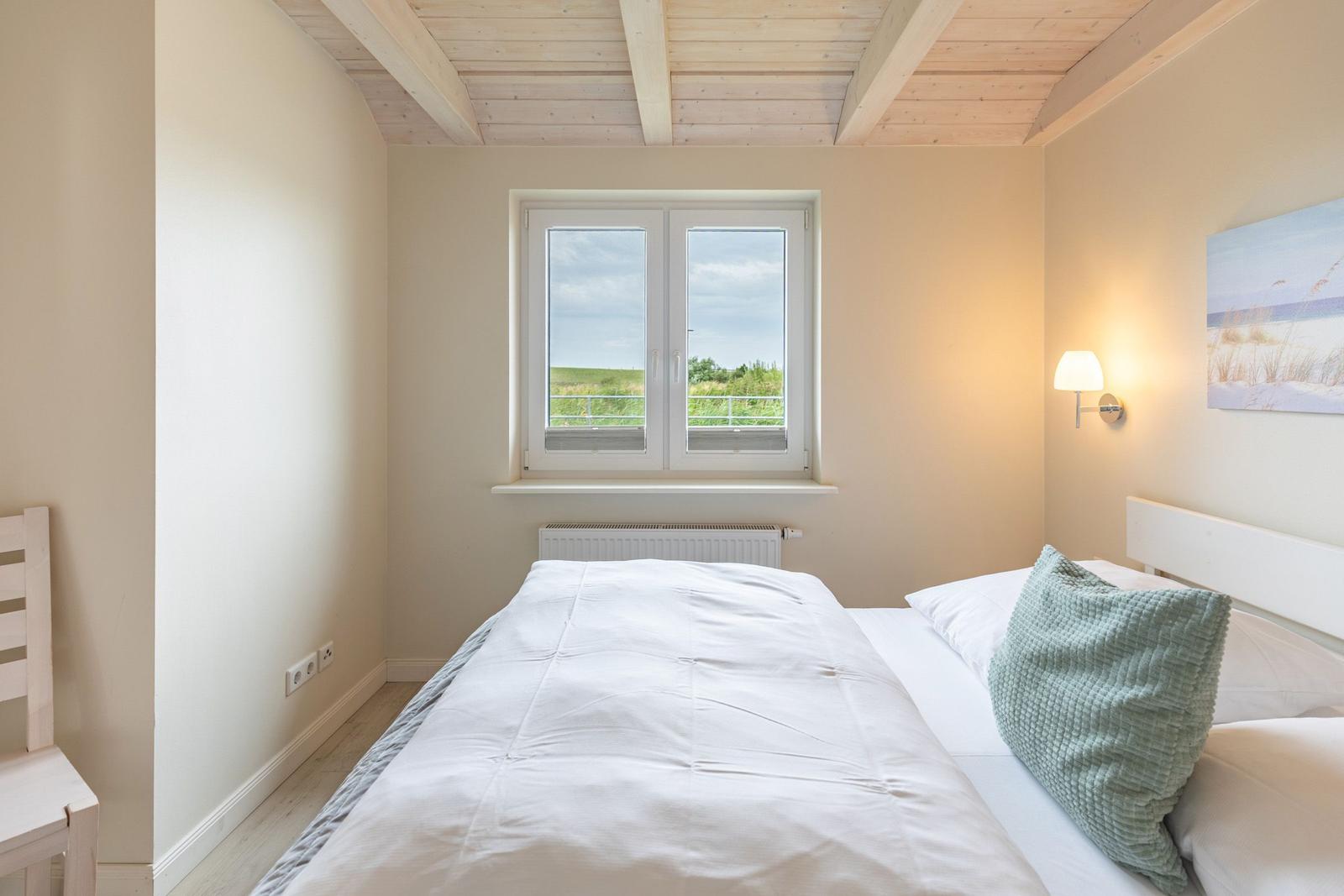 Schlafzimmer mit Doppelbett, Fenster und Holzdecke.