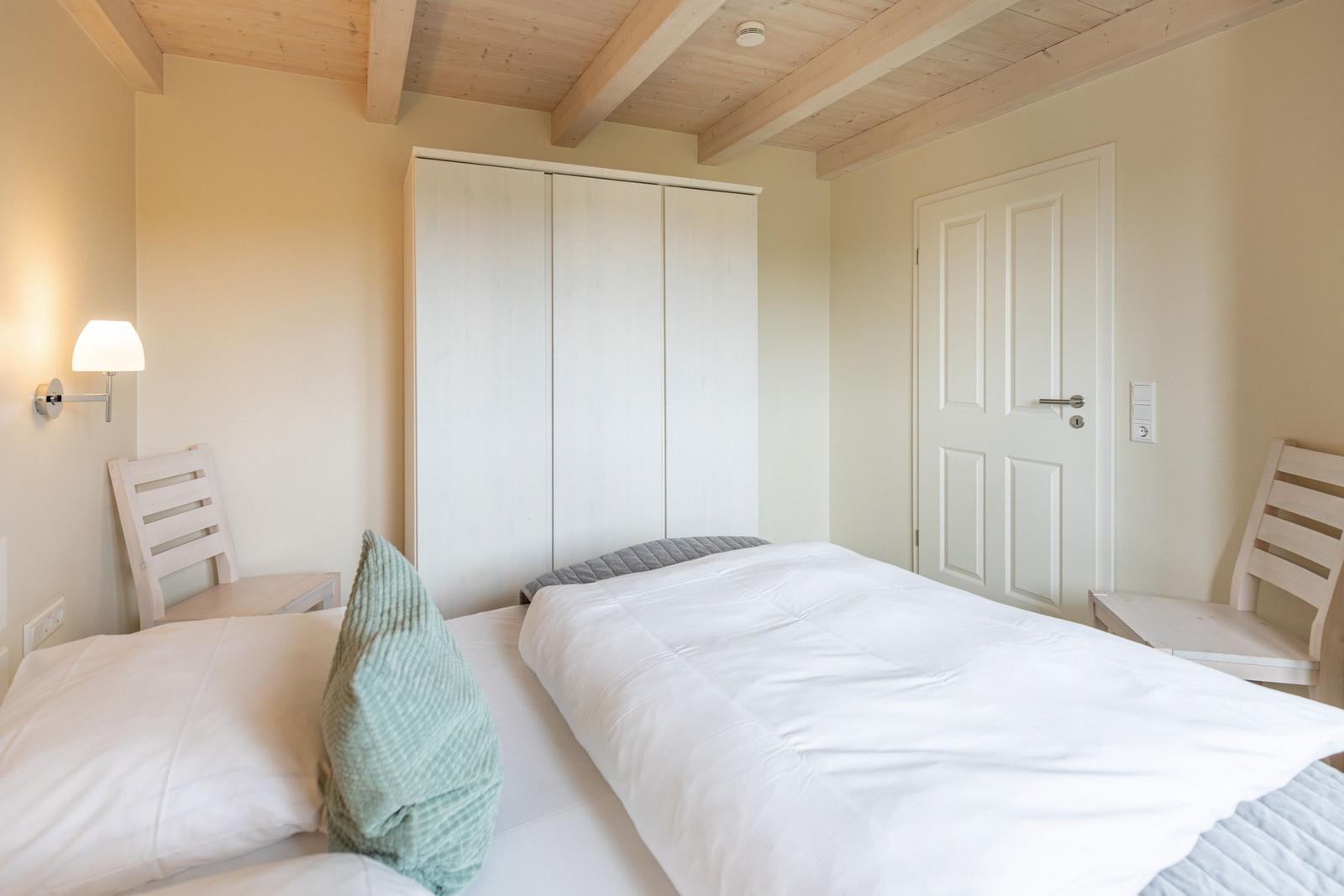 Schlafzimmer mit Bett, Kleiderschrank und zwei Stühlen an den Betten.