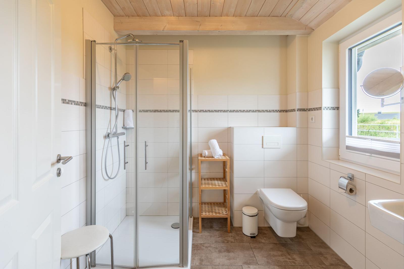 Badezimmer mit Dusche, WC und Fenster. Holzdecke und Waschbecken.