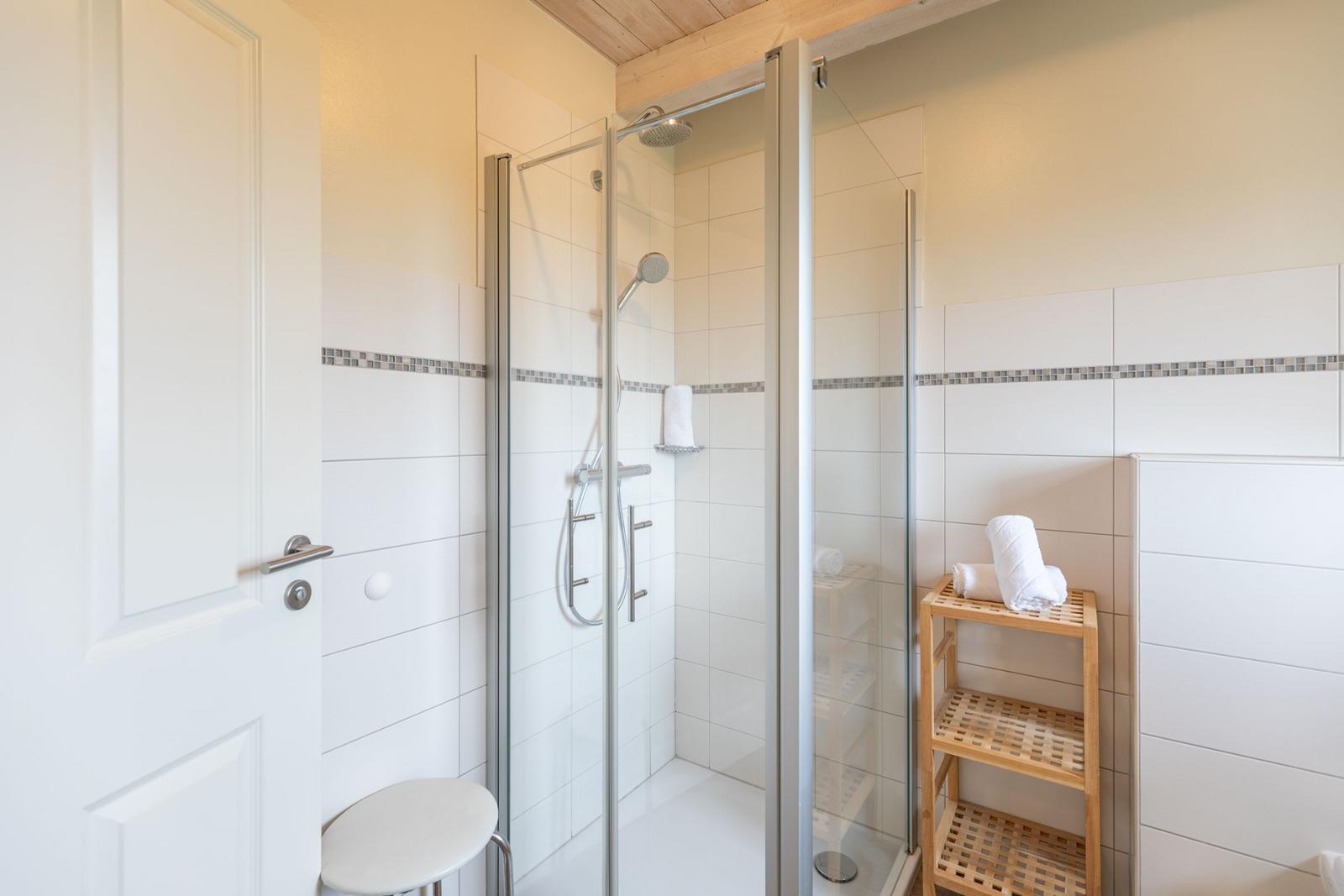 Dusche mit Glaswand, Holzregal und weißen Fliesen.