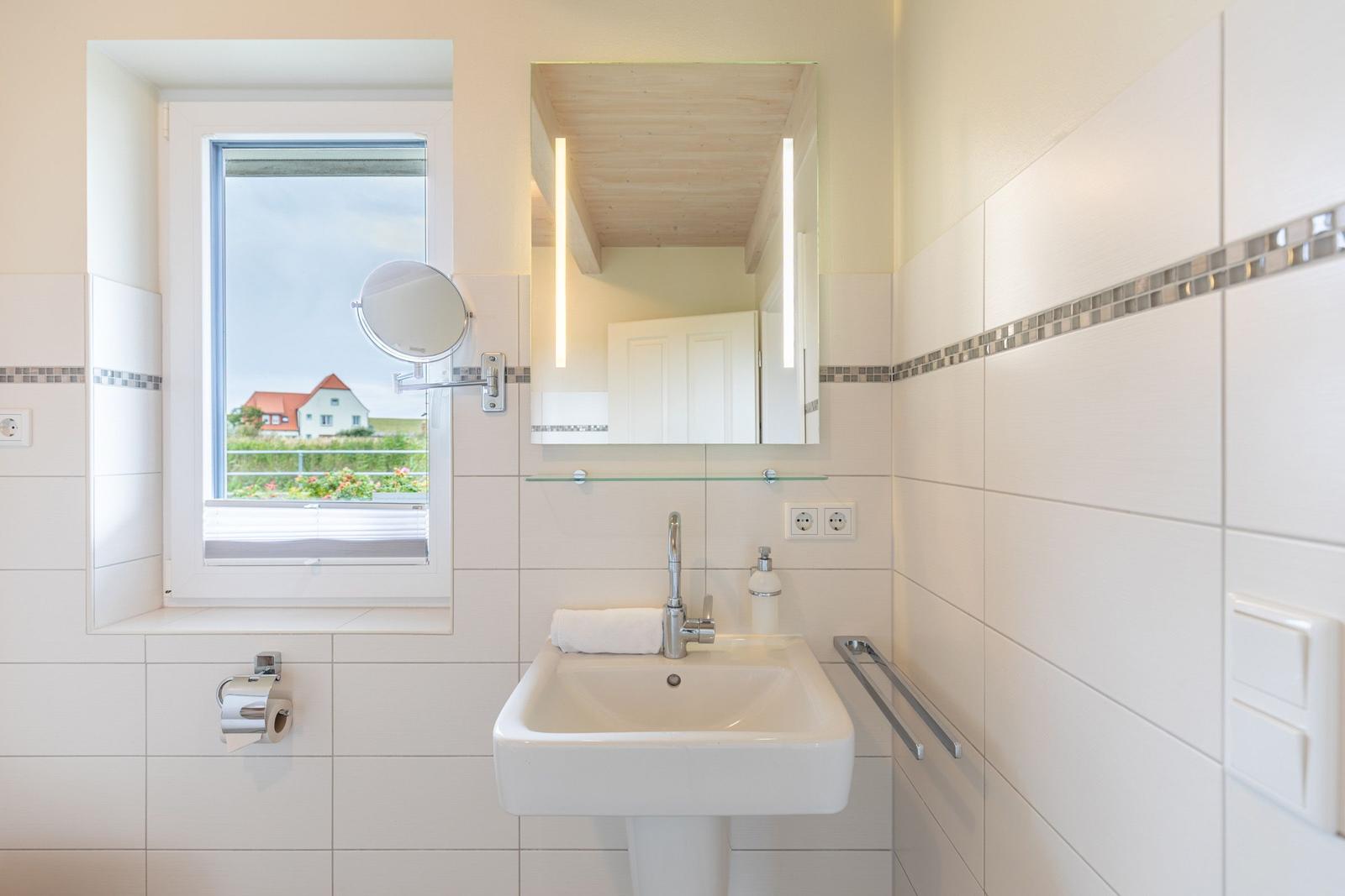 Badezimmer mit Waschbecken, Spiegel und Fensterblick auf Haus und Garten.