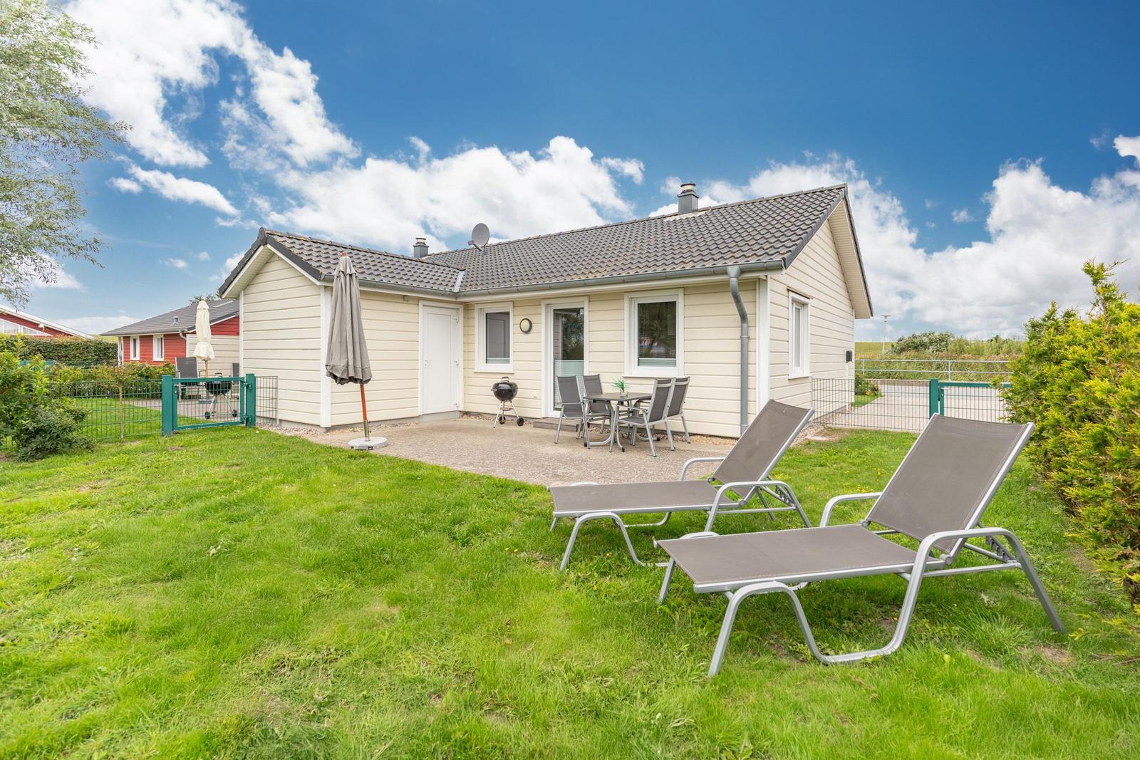 Wohnhaus mit Garten, Liegestühlen und Grillplatz unter blauem Himmel.