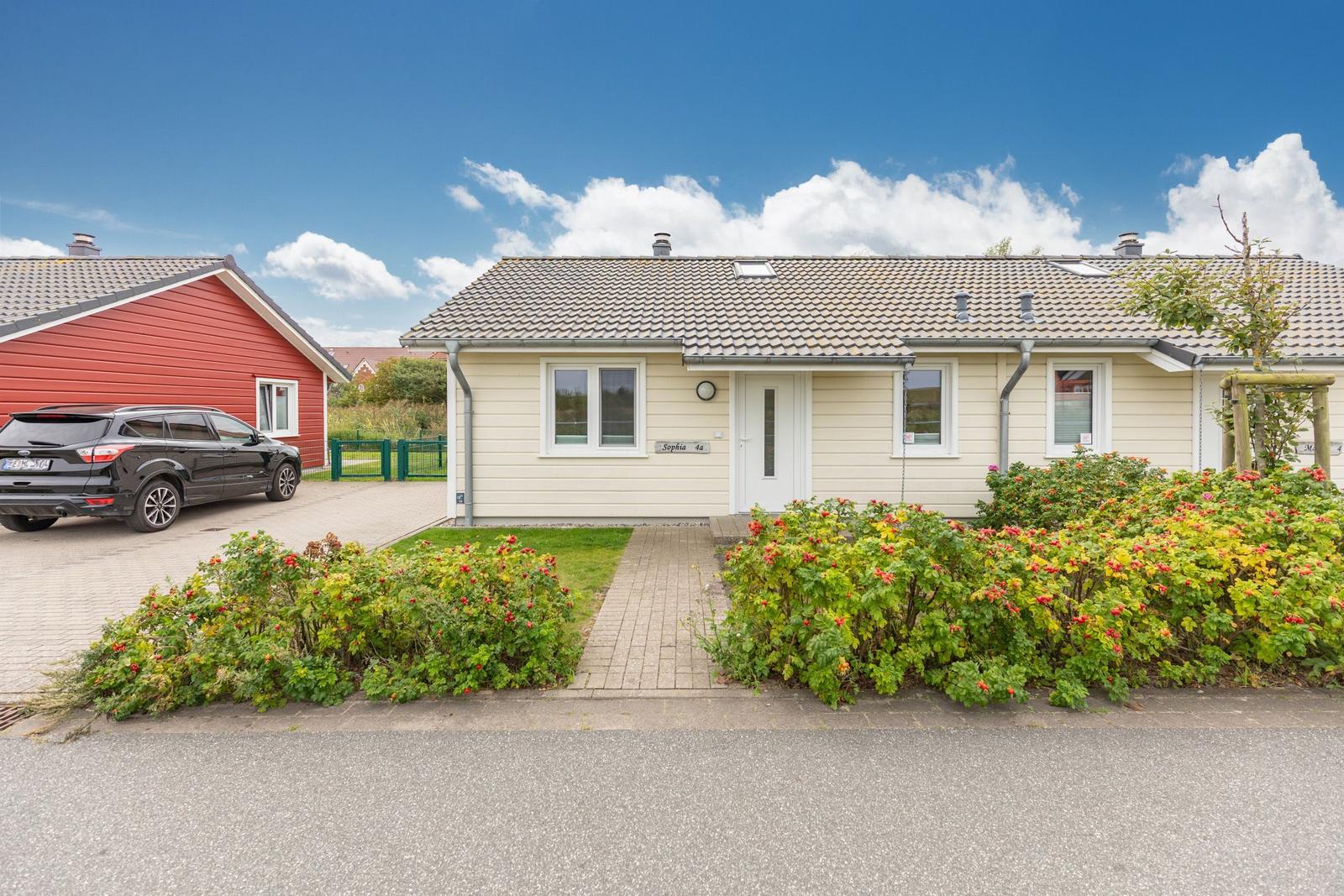 Ein hellgelbes Ferienhaus mit Garten und Parkplatz. Ein schwarzes Auto steht vorne.