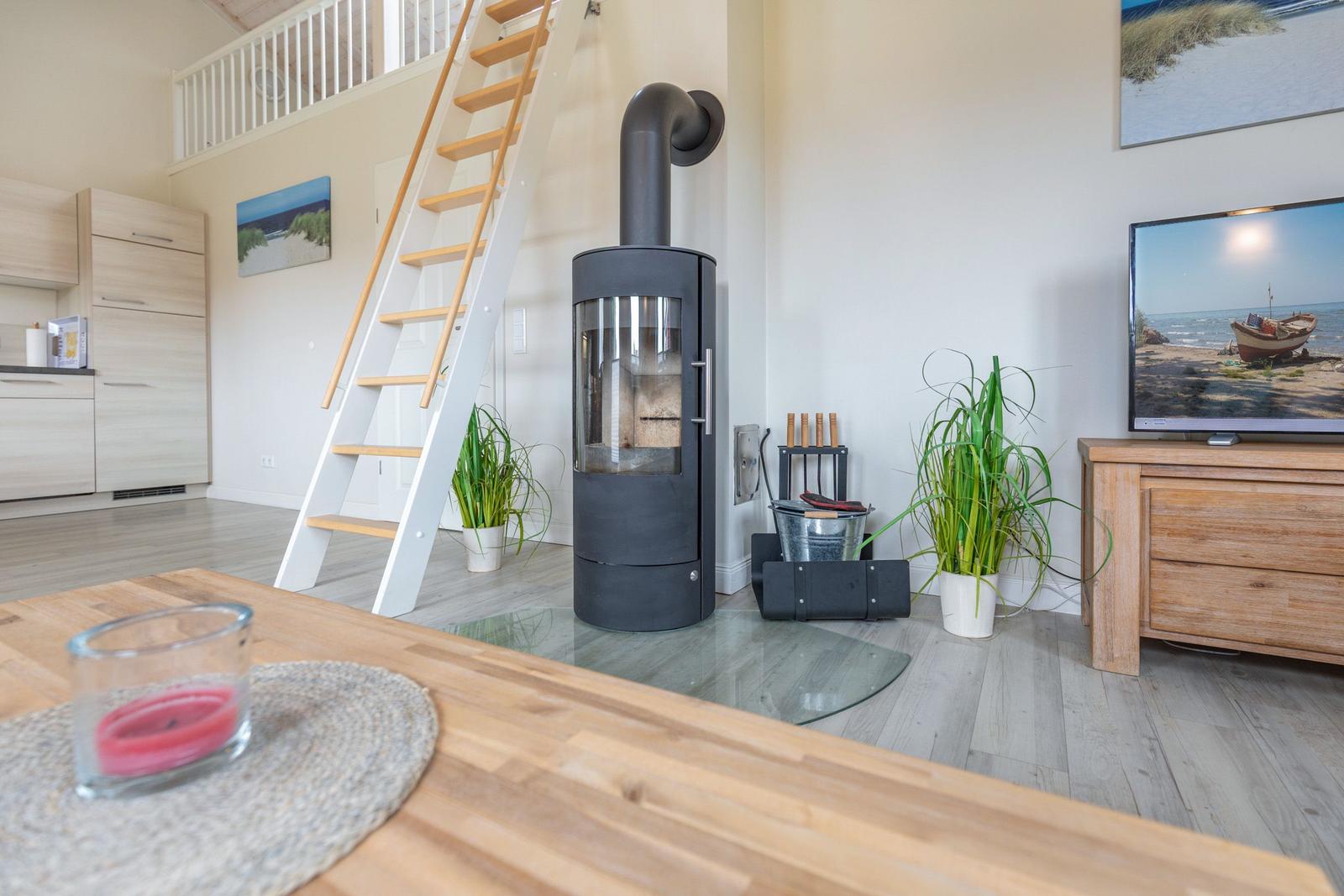 Wohnbereich mit Holzofen, Fernseher und Treppe zur Galerie.