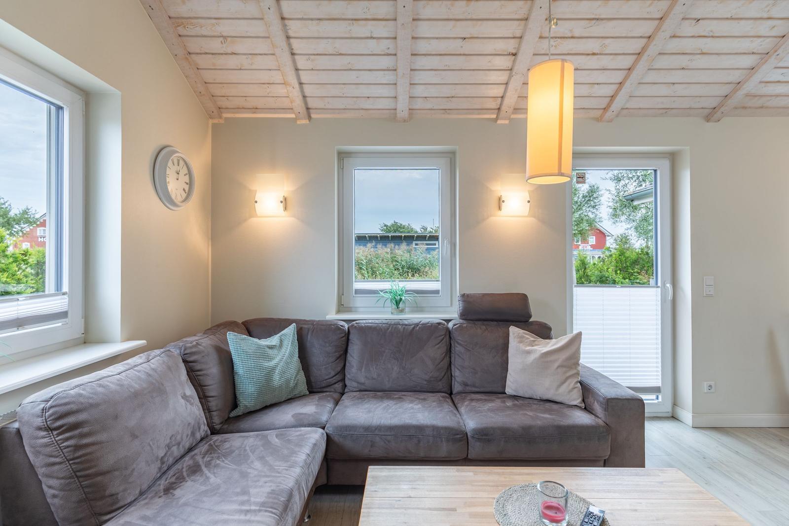 Wohnzimmer mit Ecksofa, Holzdecke und Fenstern zum Garten.