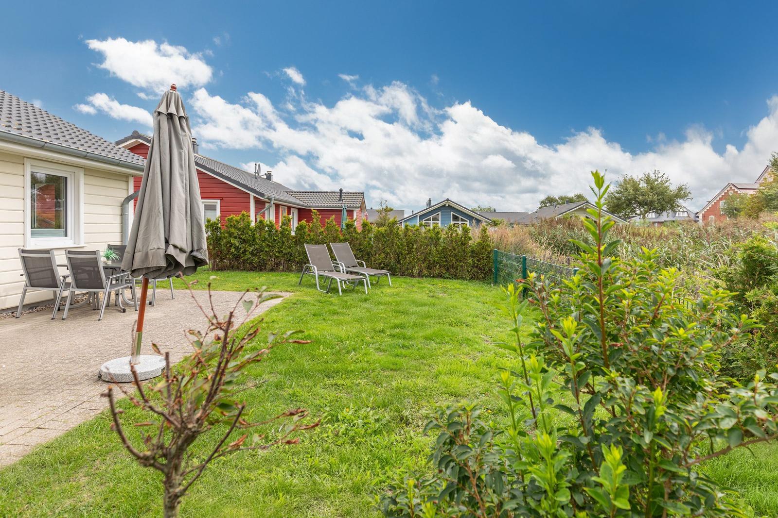 Hinterhof mit Garten, Liegestühlen und Terrasse unter blauem Himmel.