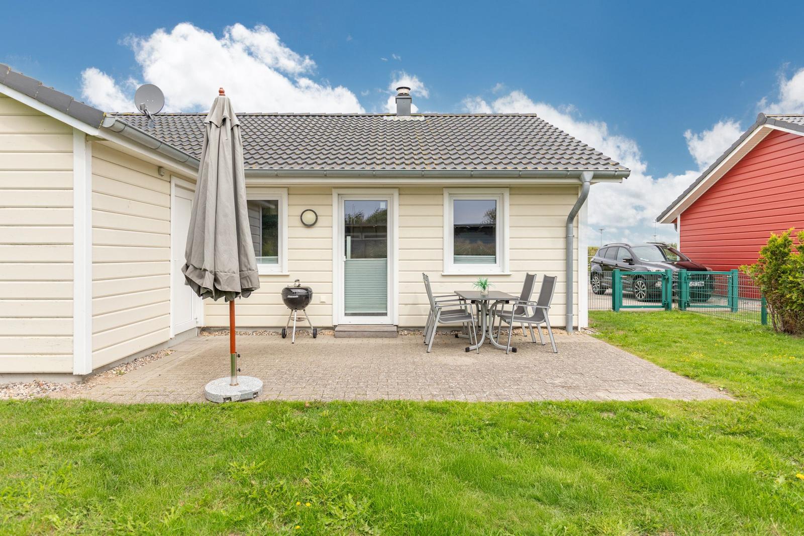 Haus mit Terrasse, Grill und Garten. Nebenhaus und Auto sind sichtbar.