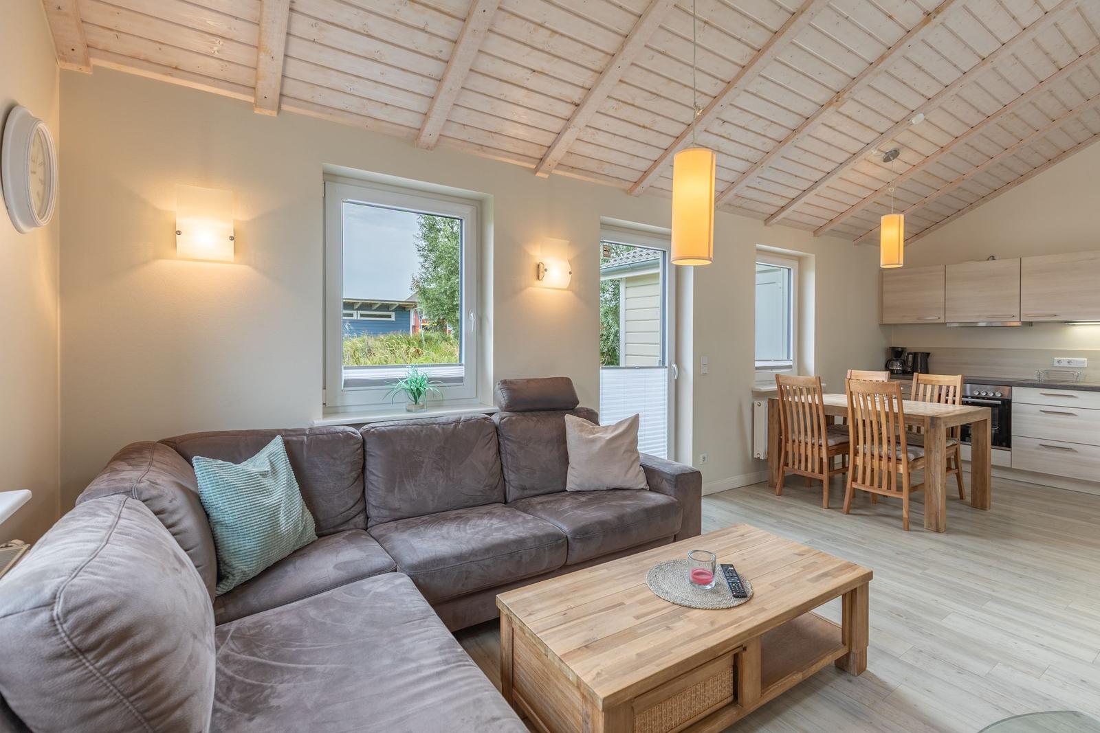 Wohnbereich mit Sofa, Esstisch und Küchenzeile unter Holzdecke.