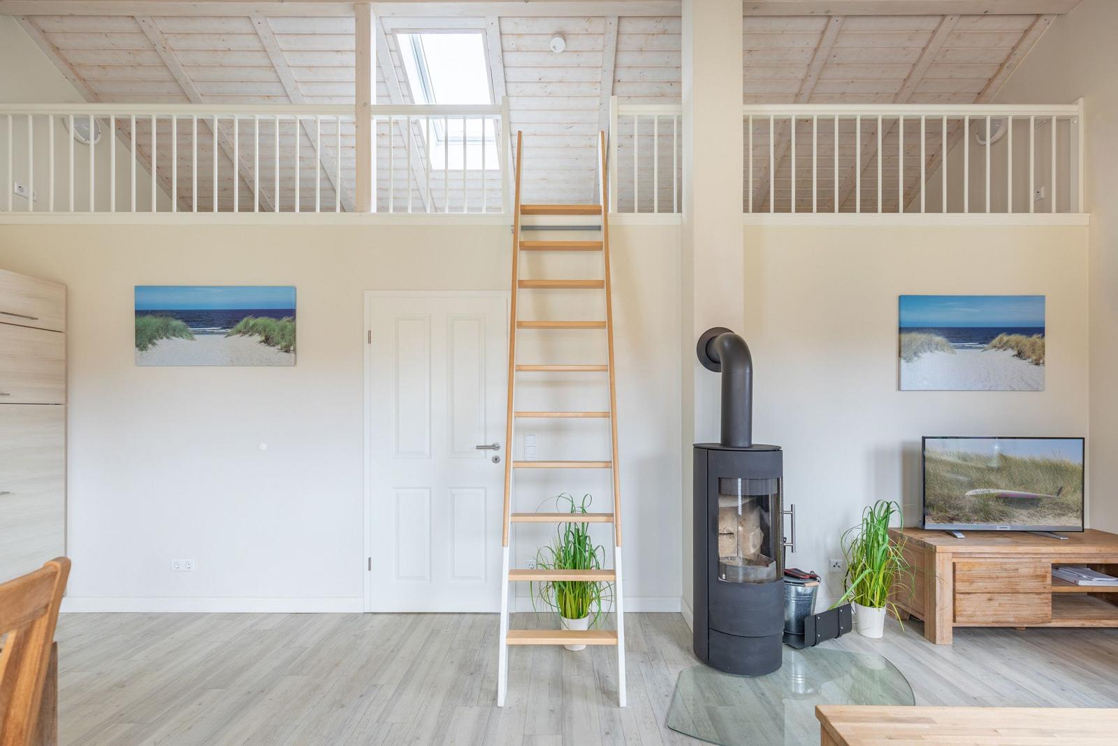 Wohnraum mit Holztreppe zur Galerie, Kamin und TV.