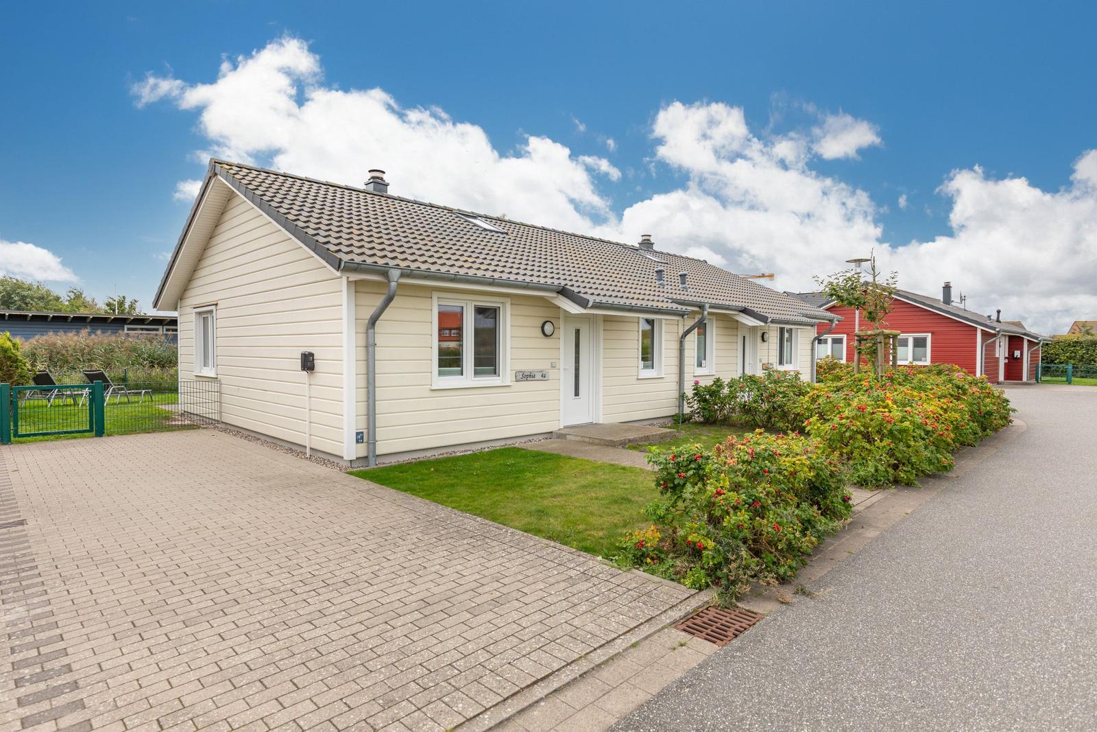 Ein hellbeiges Ferienhaus mit Garten und Terrasse unter blauem Himmel.