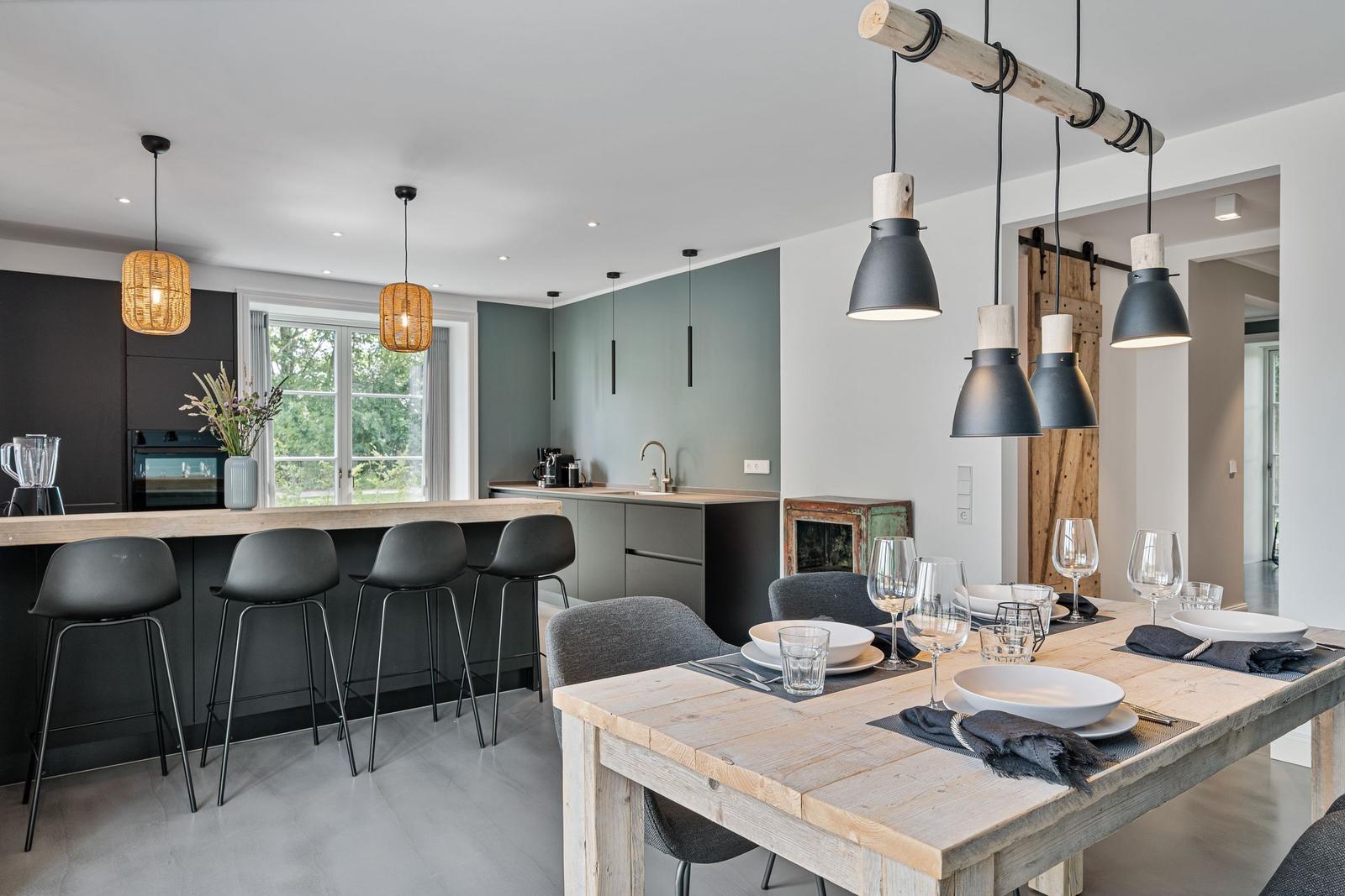 Essbereich mit rustikalem Tisch und moderner Küche mit Barhocker.