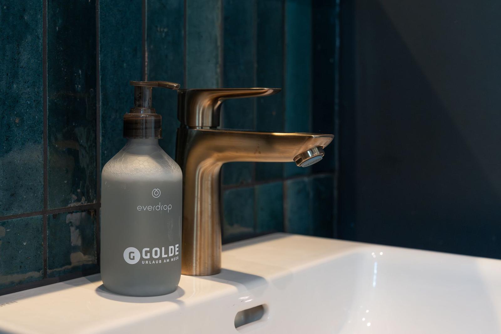 Waschbecken mit goldenem Wasserhahn und Seifenspender.