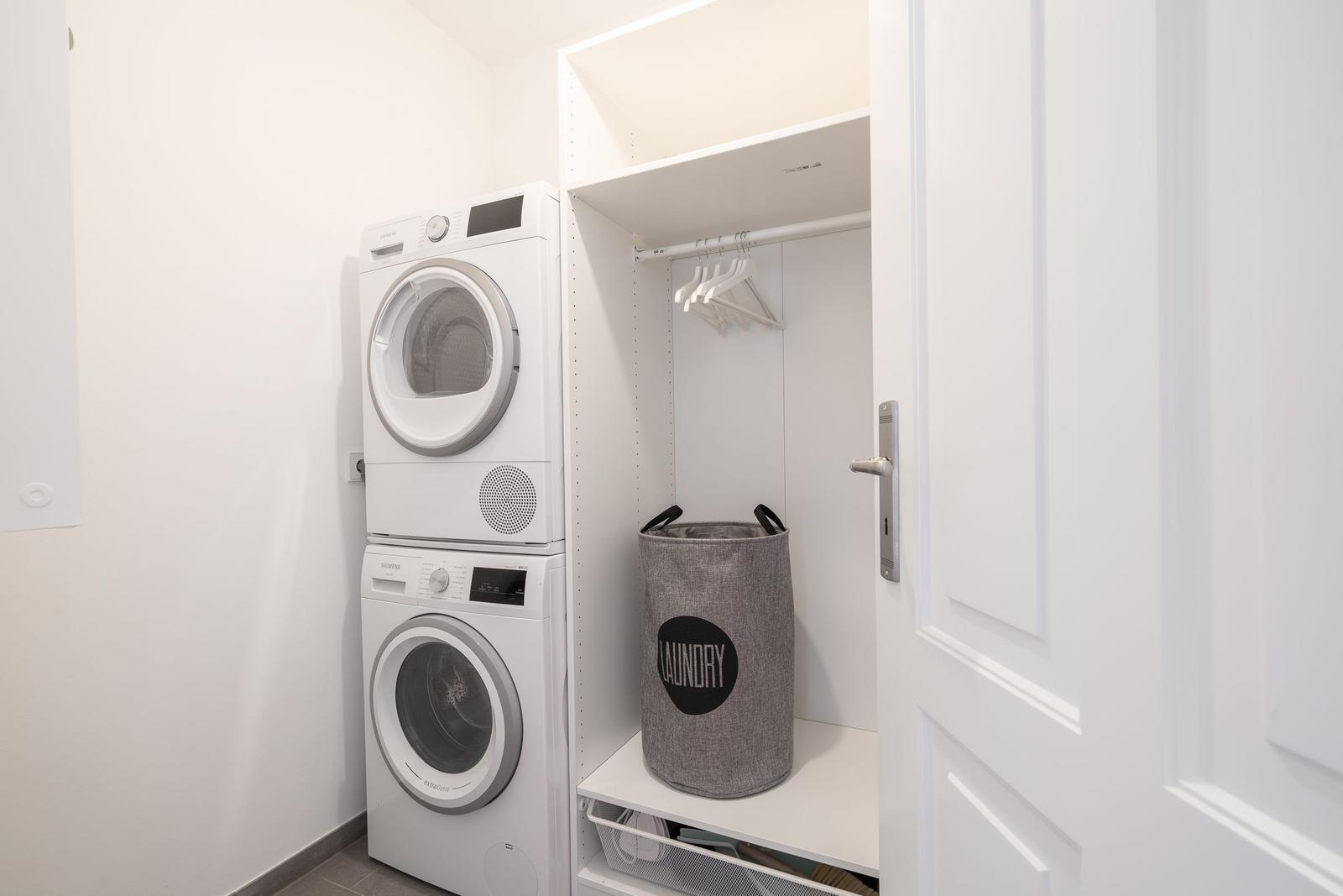 Waschmaschine und Trockner in weißer Wandnische mit Kleiderständer und Wäschekorb.