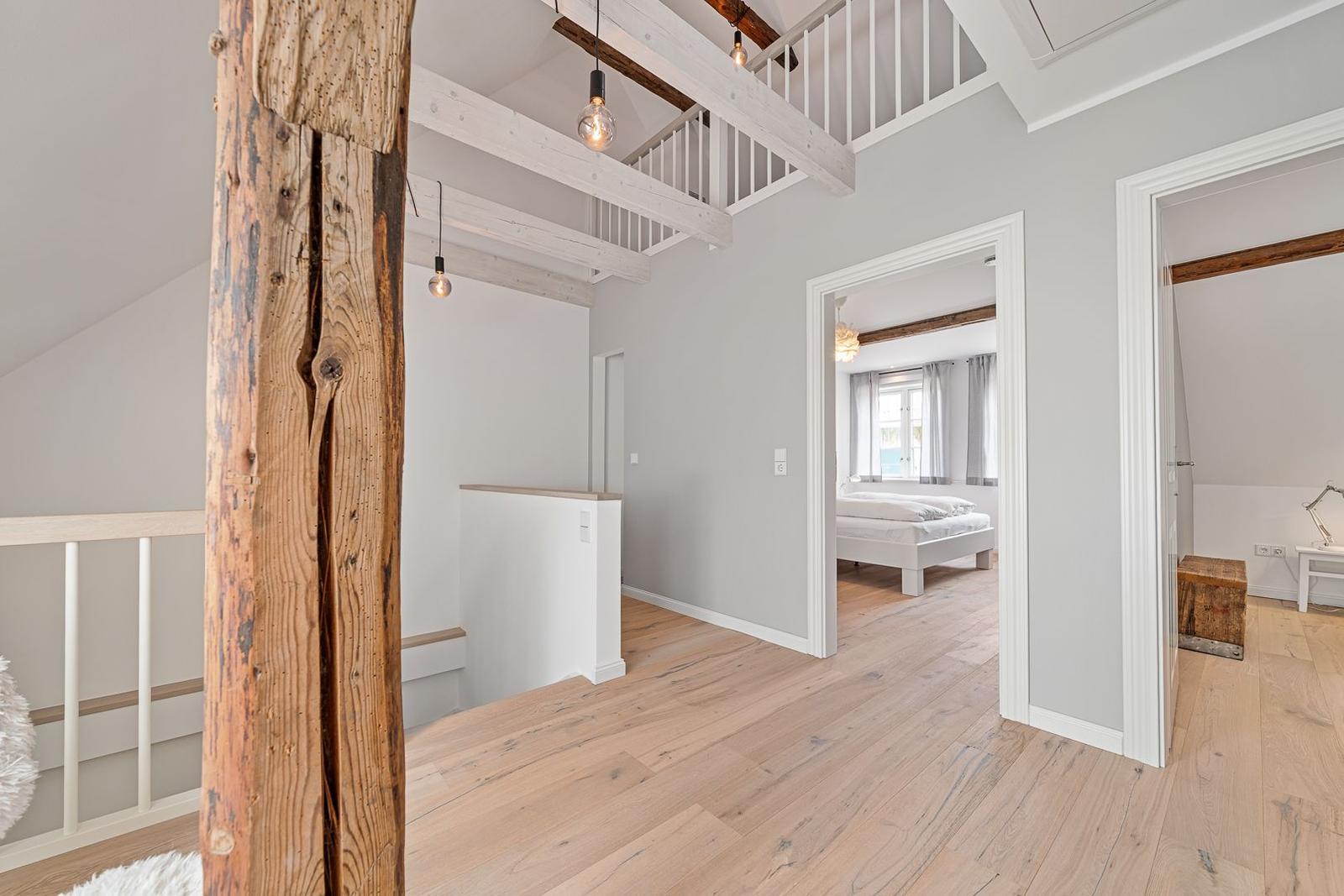 Haus mit Holzdielen, Balken und Schlafzimmer im Hintergrund.
