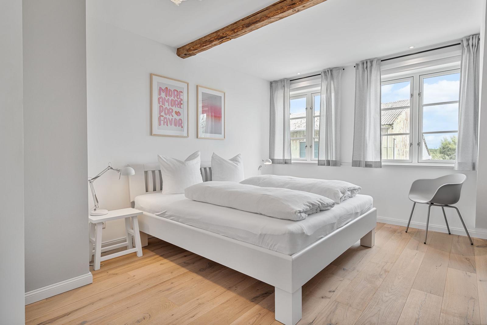 Schlafzimmer mit weißem Bett, Holzboden und Fenster mit Blick.