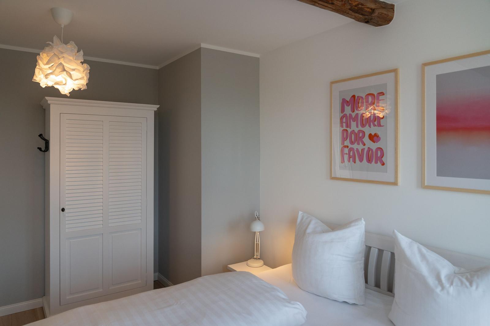 Schlafzimmer mit Bett, Schrank und Wandbildern.