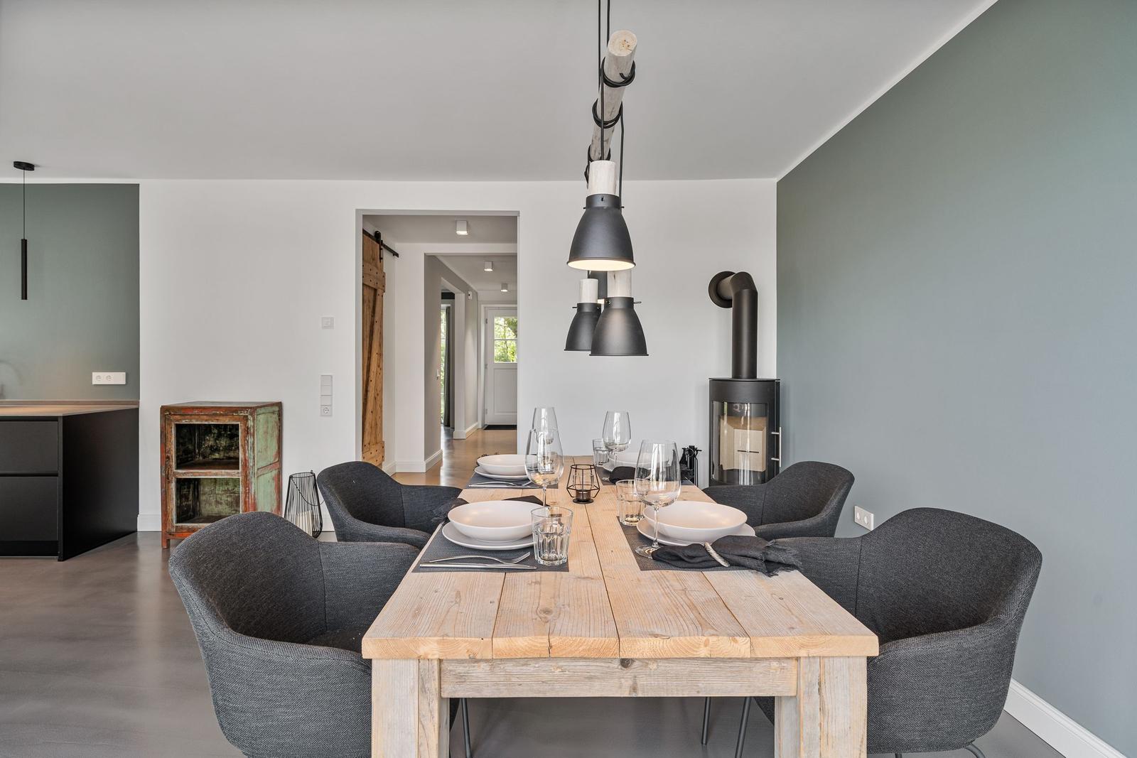 Esstisch mit sechs Stühlen und Holzoberfläche. Hängelampe und Kaminofen im Hintergrund.