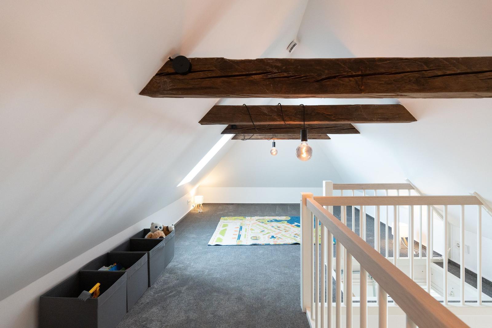 Dachgeschosszimmer mit Spielteppich, Holzbalken und Spielzeugboxen