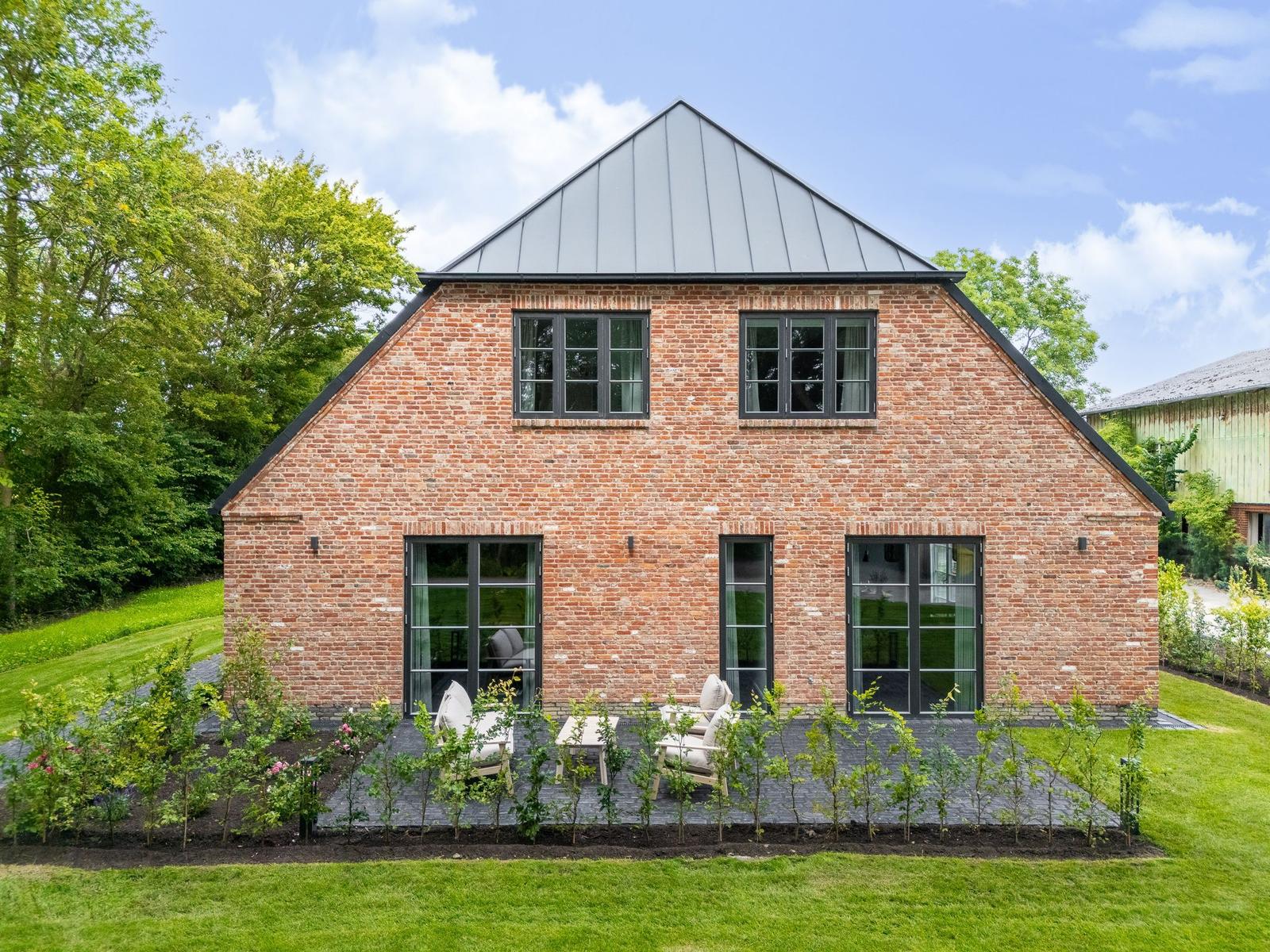Rotes Backsteinhaus mit dunklen Fenstern und Terrasse im Garten.
