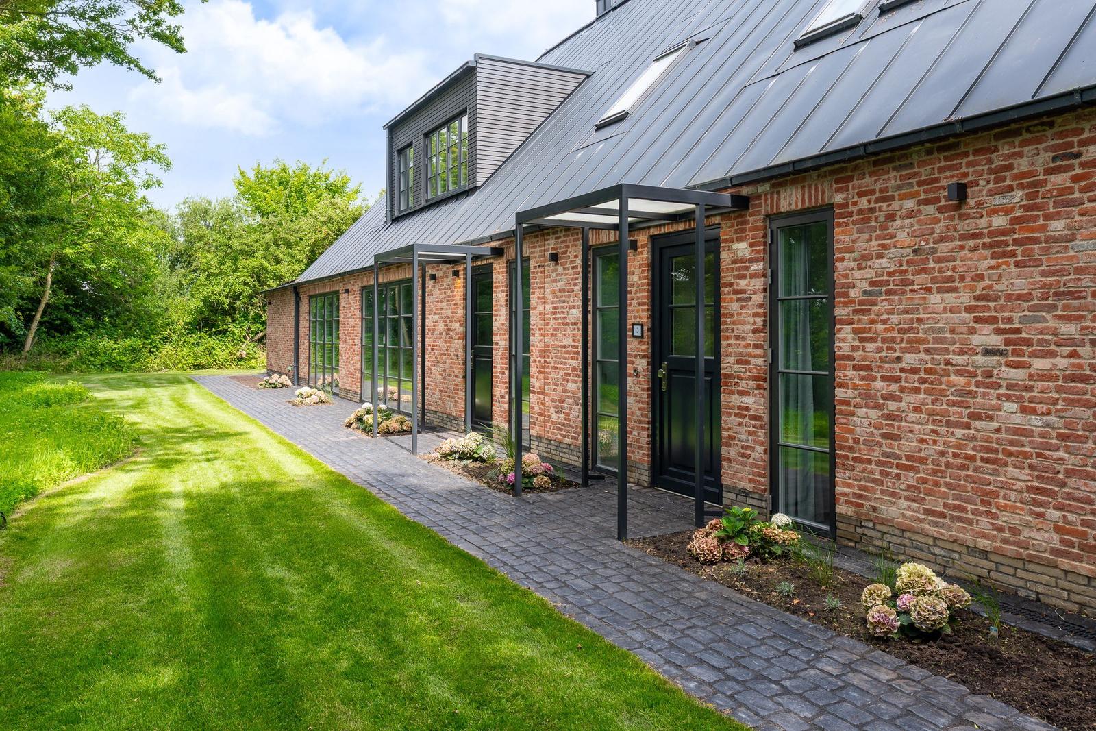Rotes Backsteinhaus mit schwarzem Dach und Glasfronten. Pflasterweg und grüner Rasen.