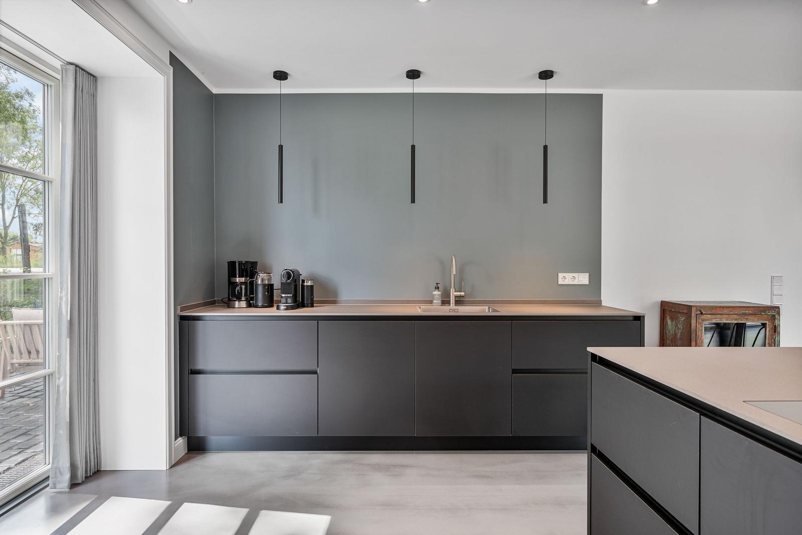 Moderne Küche mit grauen Schränken, Arbeitsplatte und Fensterblick.