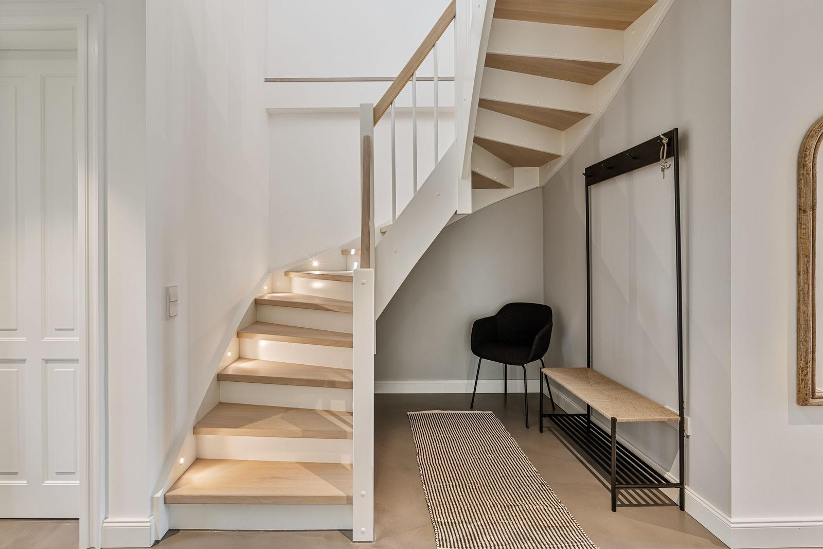 Treppe mit Holzstufen und moderner Beleuchtung. Eingangsbereich mit Sitzgelegenheit und Kleiderständer.