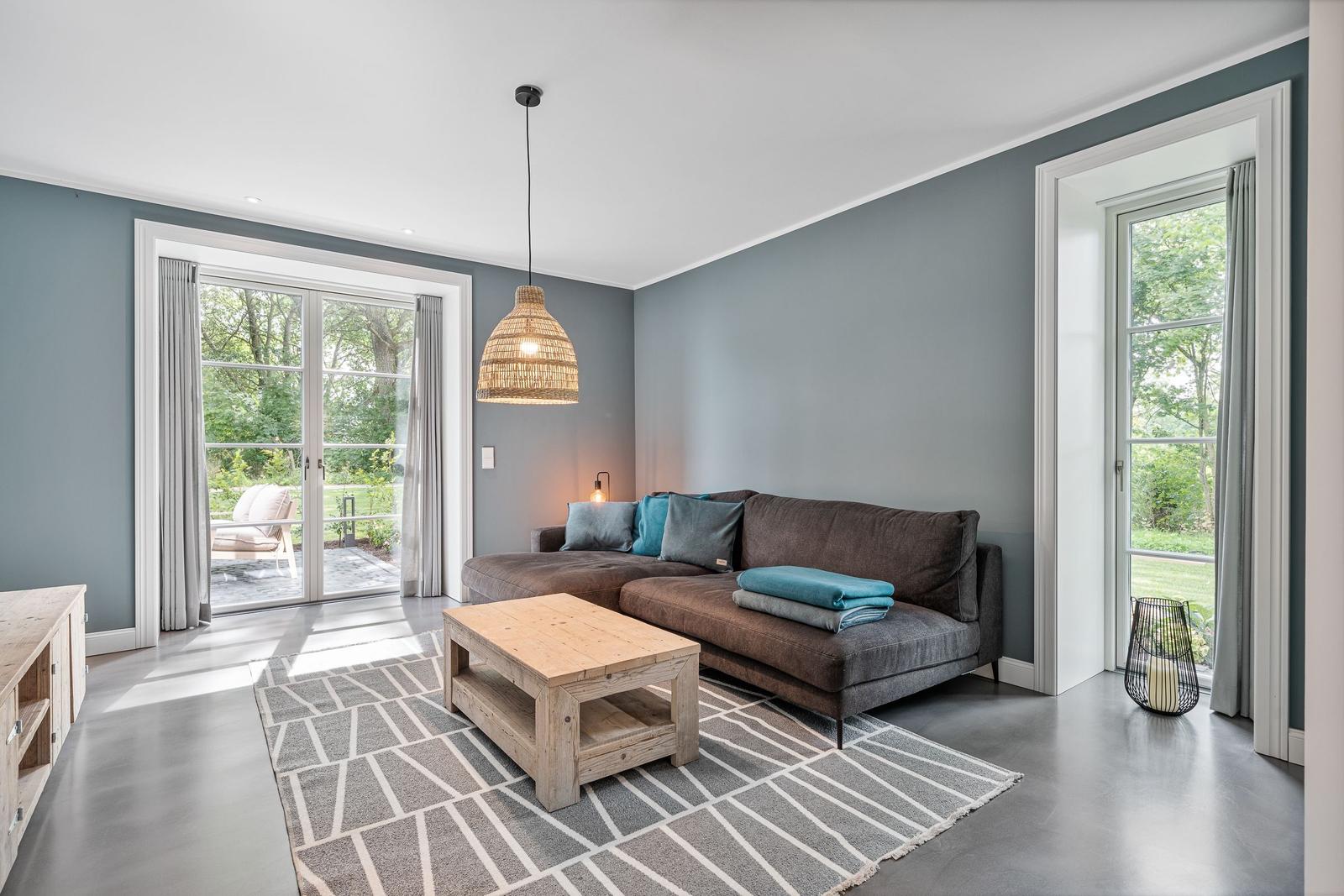 Wohnzimmer mit Sofa, Tisch und Fenstern zum Garten.