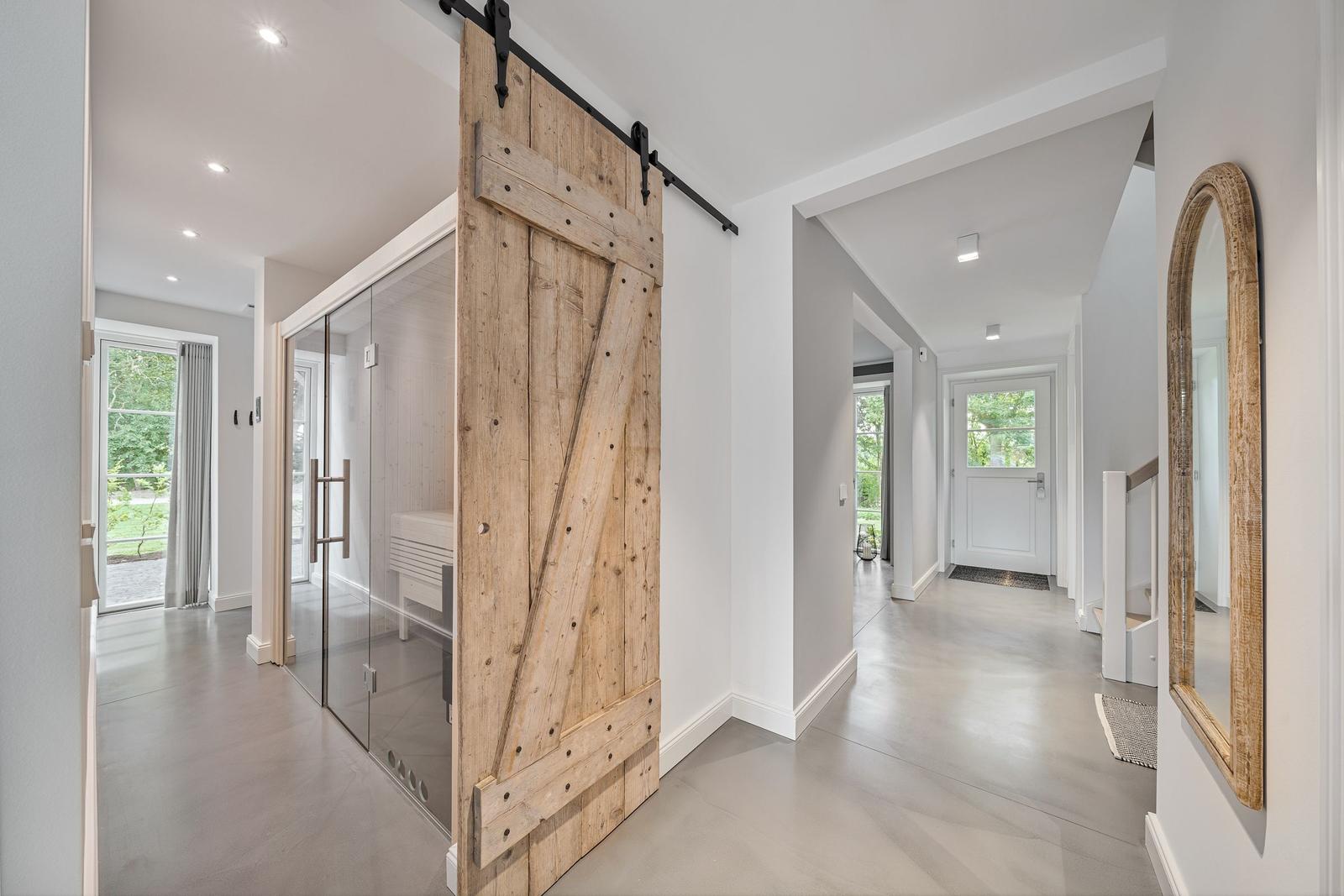 Eingangsbereich mit Holzschwingtür und Glaswand. Helle Wände und Boden.