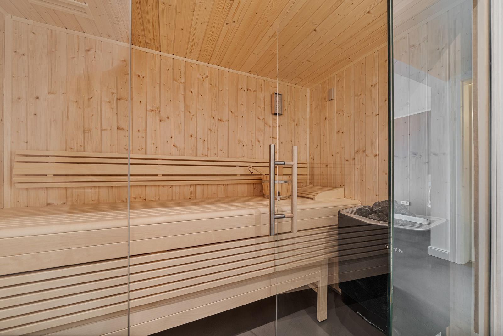 Sauna mit Holzbank und Glaswand. Heizung und Eimer sind sichtbar.