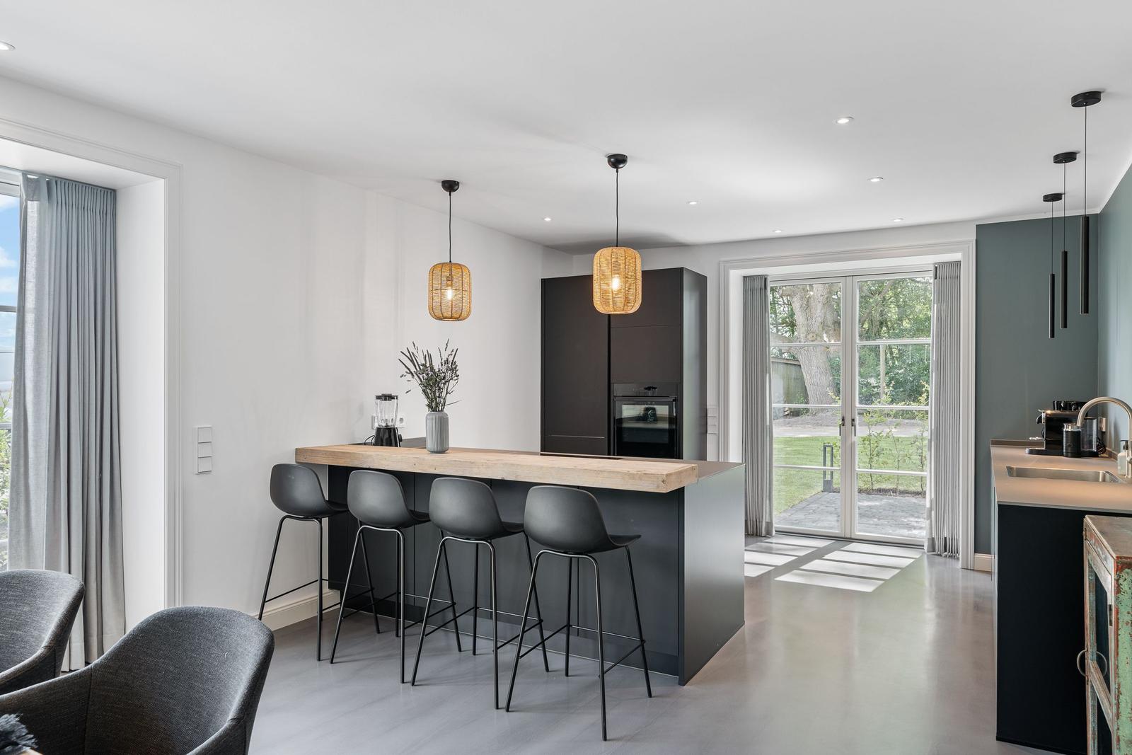 Moderne Küche mit Kücheninsel und Sitzgelegenheit. Durchgang zur Terrasse mit Gartenansicht.