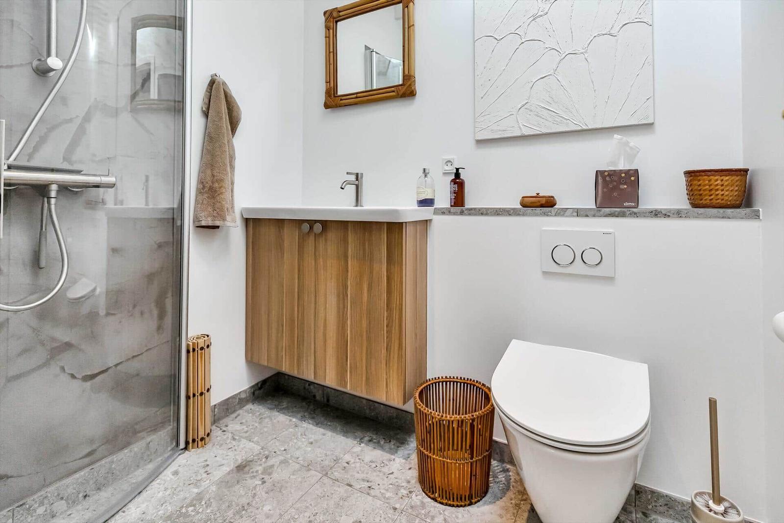 Badezimmer mit Dusche, Waschbecken und Toilette. Holzschrank, Spiegel und Wandbild.