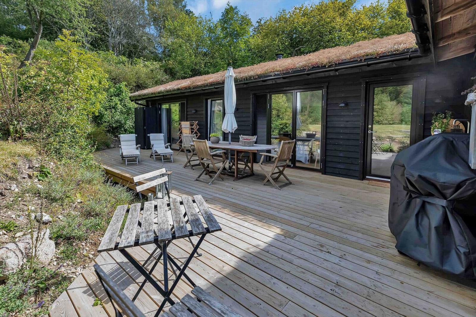Terrasse mit Tisch, Stühlen und Grill. Holzhaus mit grüner Umgebung.