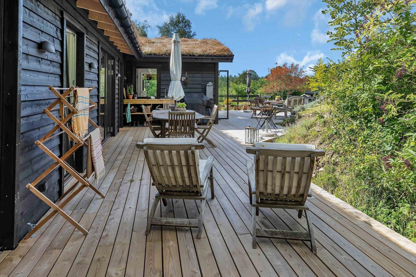 Terrasse mit Holzdielen, Stühlen und Blick auf grüne Landschaft.