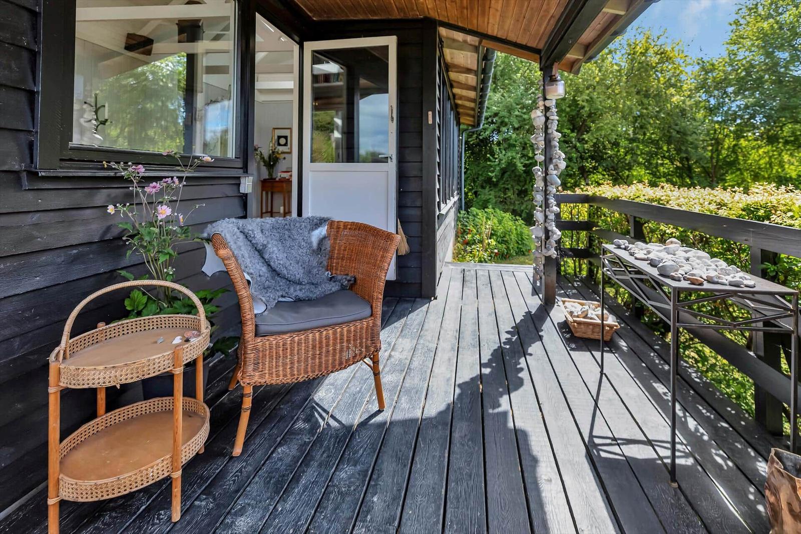 Terrasse mit Stuhl, Tisch und Pflanzen. Hintergrund: Haus und Grün.