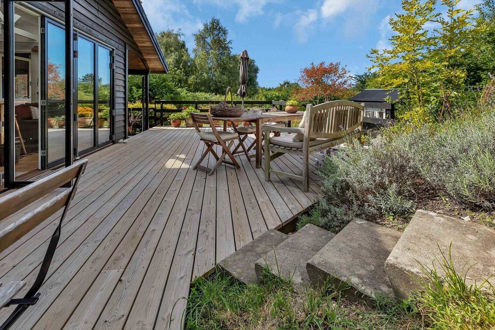 Holzterrasse mit Tisch, Stühlen und Garten. Schiebetüren führen ins Haus.