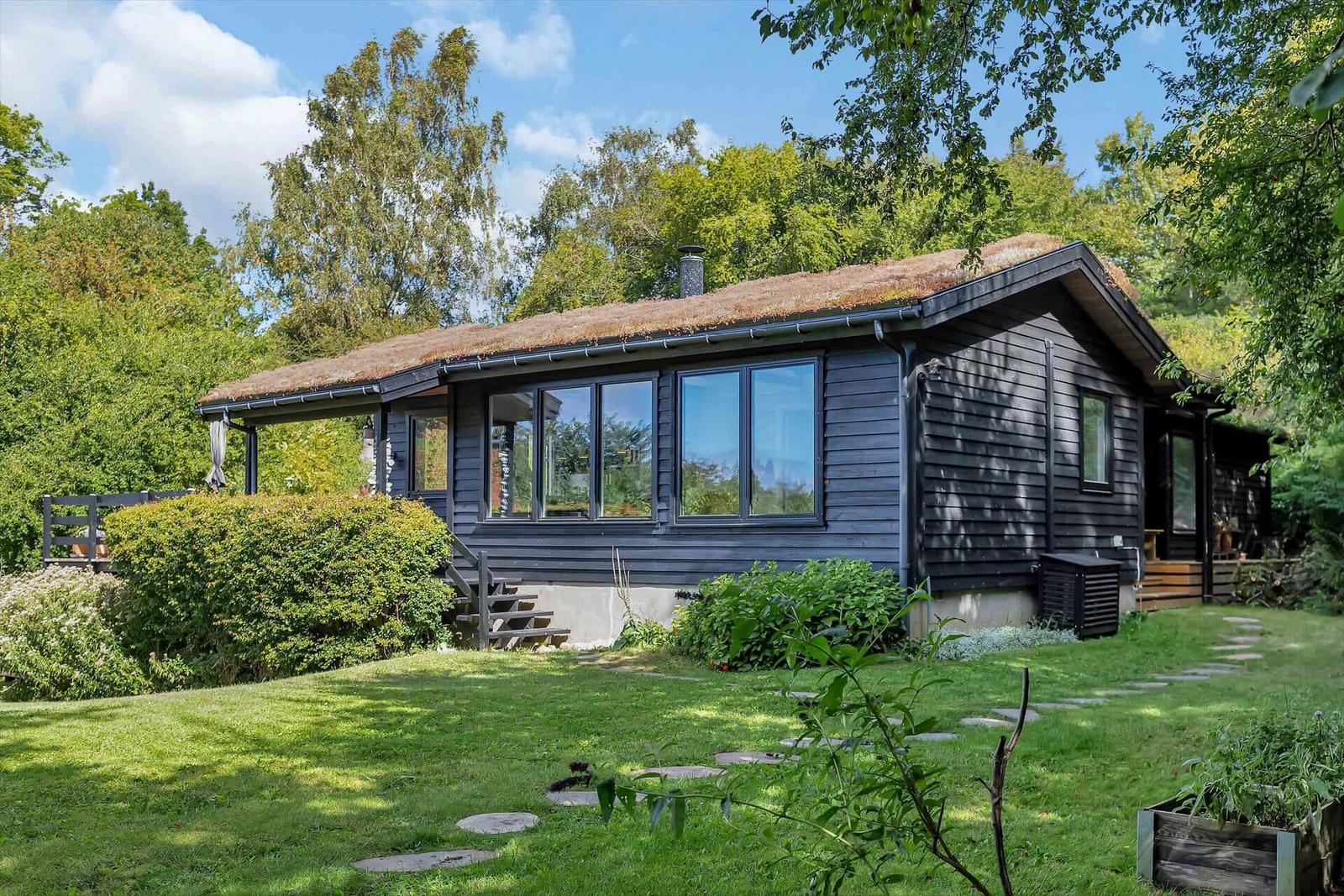 Ein Haus mit Dach aus Gras, umgeben von Grünflächen und Bäumen.