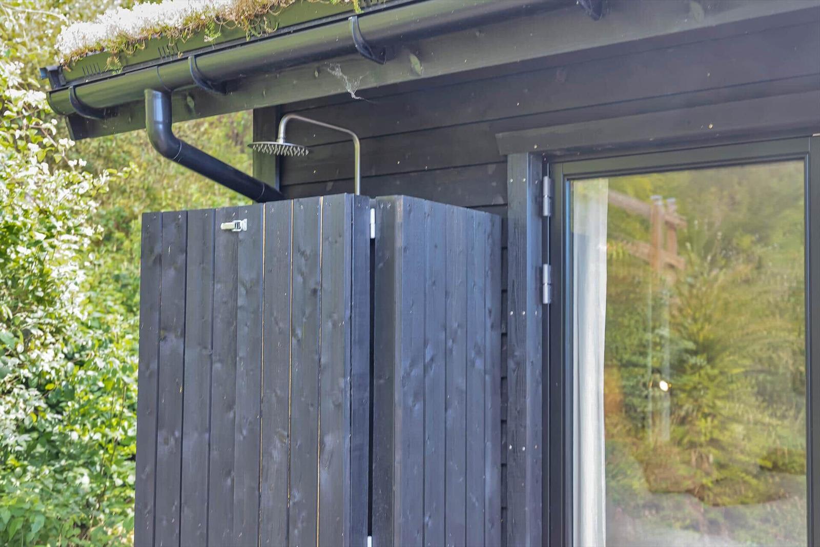 Außen-Dusche mit Holzabtrennung und Dachrinne. Grüne Umgebung sichtbar.