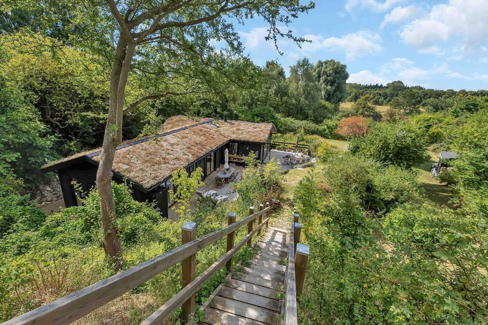 Holzsteg führt zu einem Haus mit Grasdach und Terrasse im Grünen.