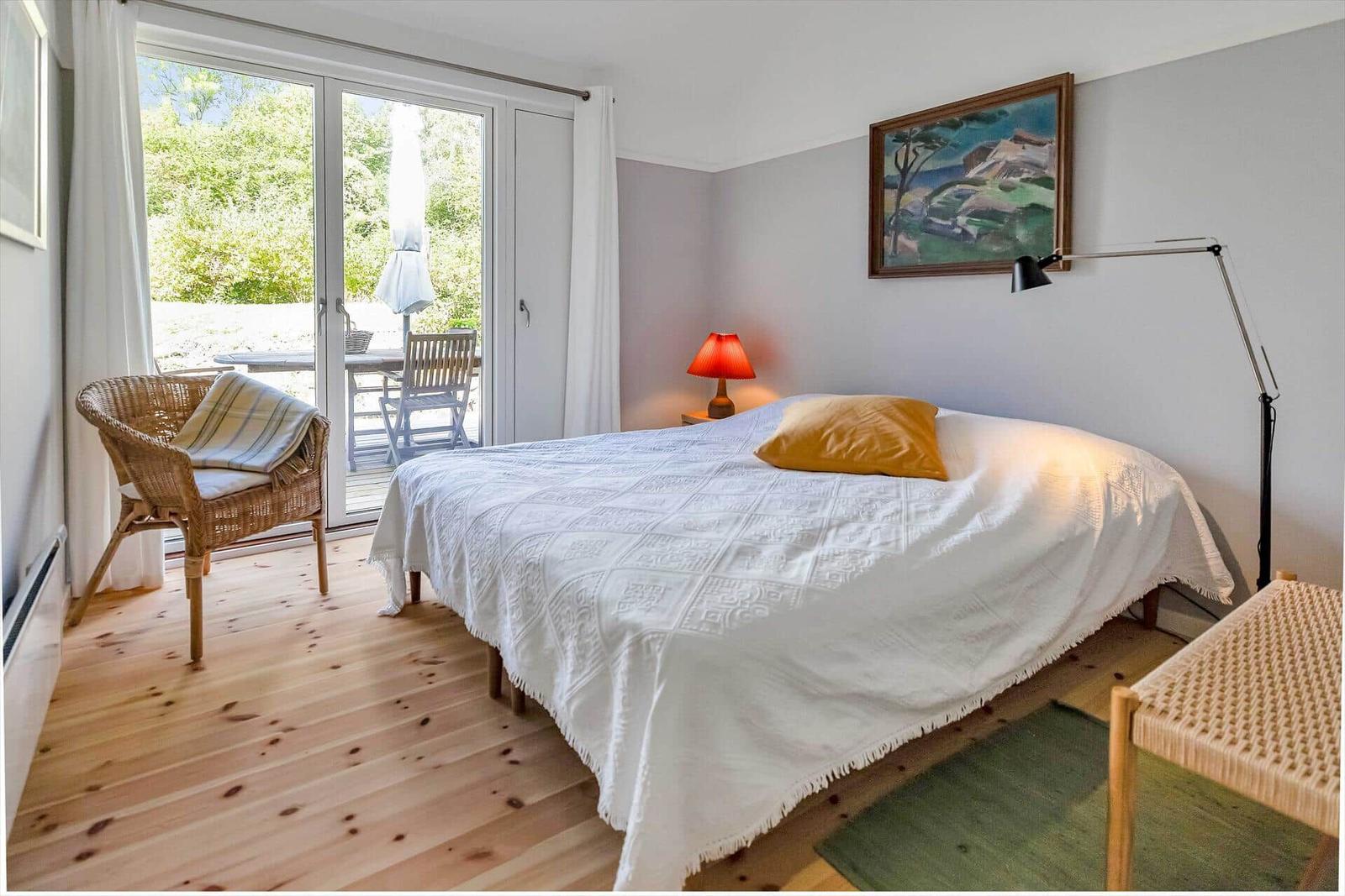 Schlafzimmer mit Bett, Stuhl und Blick auf Terrasse.