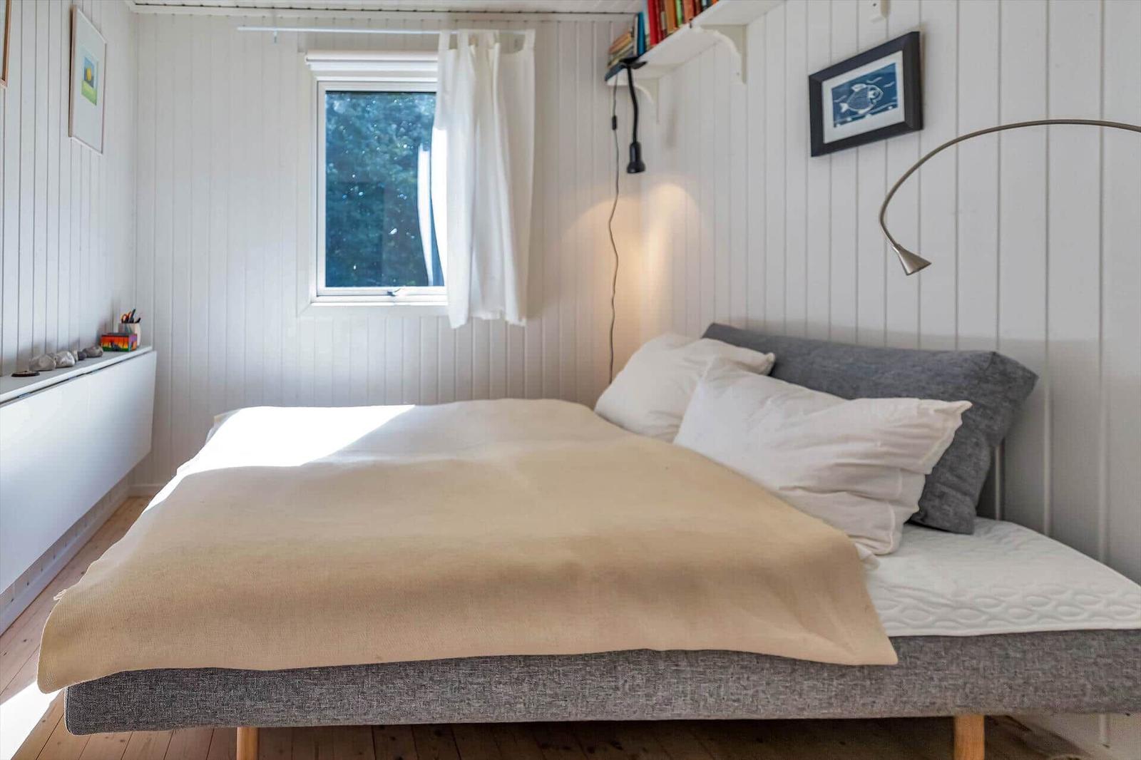 Schlafzimmer mit Bett, Fenster und Wandregal.