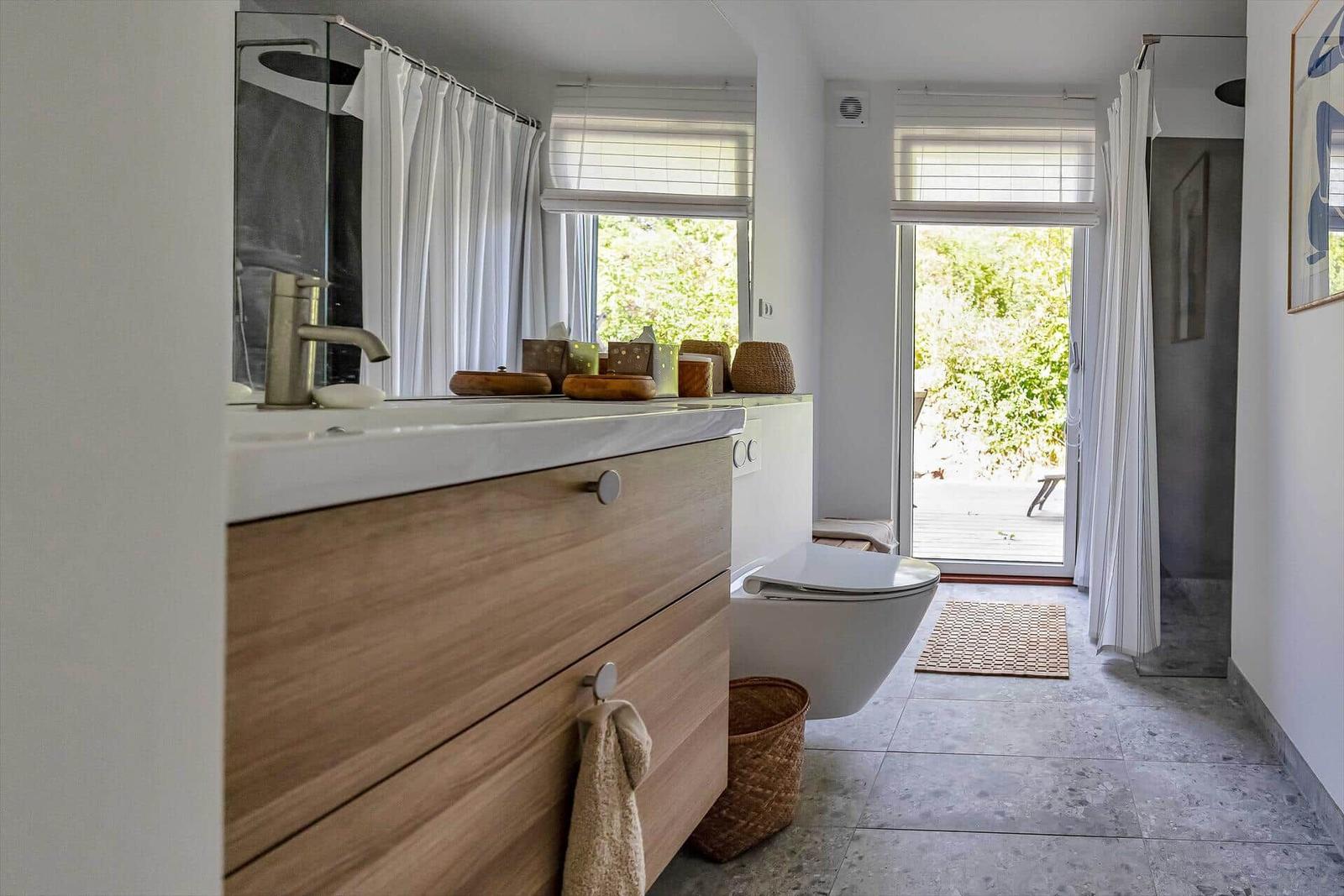 Badezimmer mit Waschbecken, Toilette und Dusche. Durchgang zur Terrasse mit Blick auf Grün.