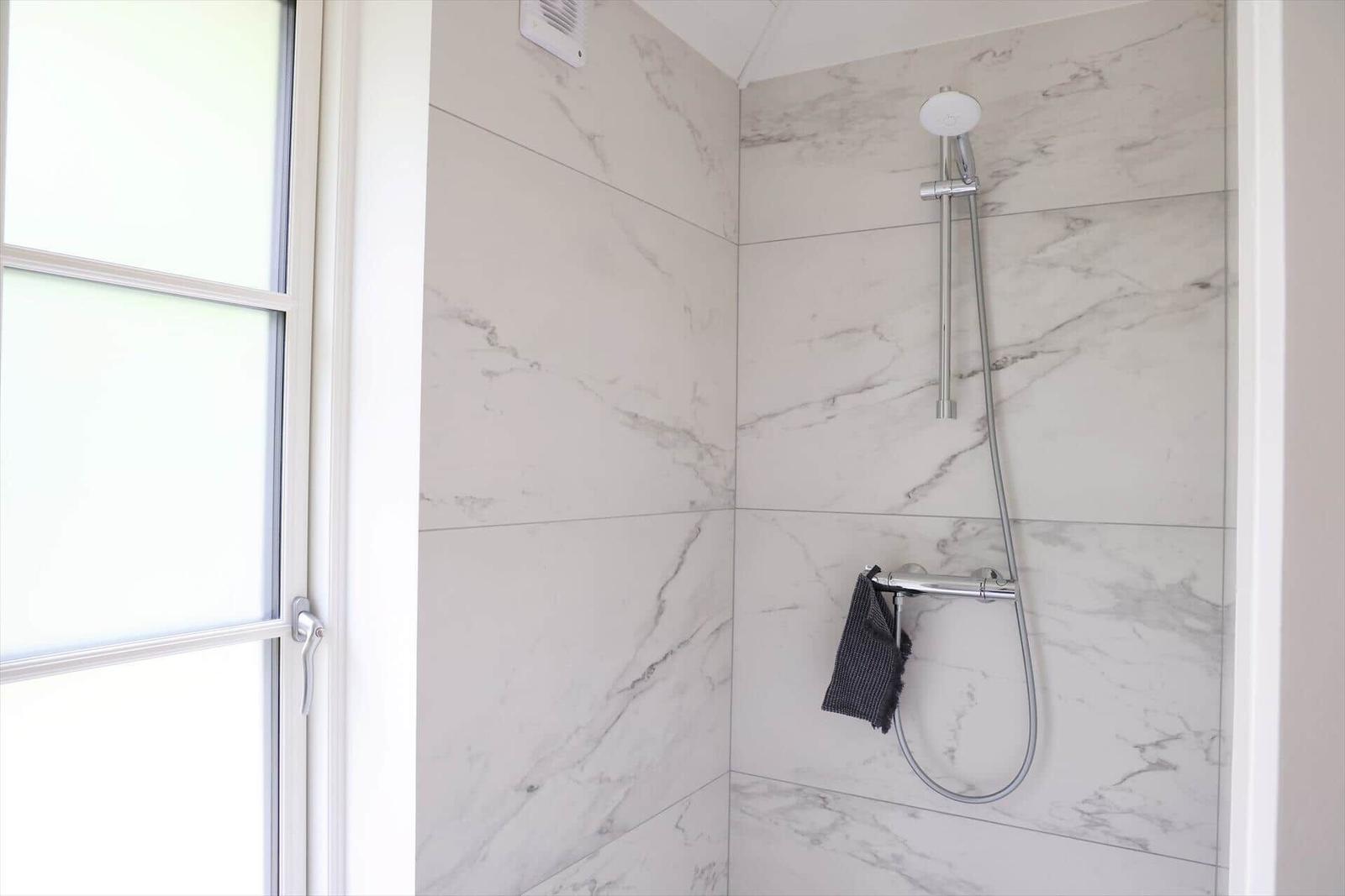 Dusche mit Marmorwand und Duschbrause. Fenster mit Glastüren.